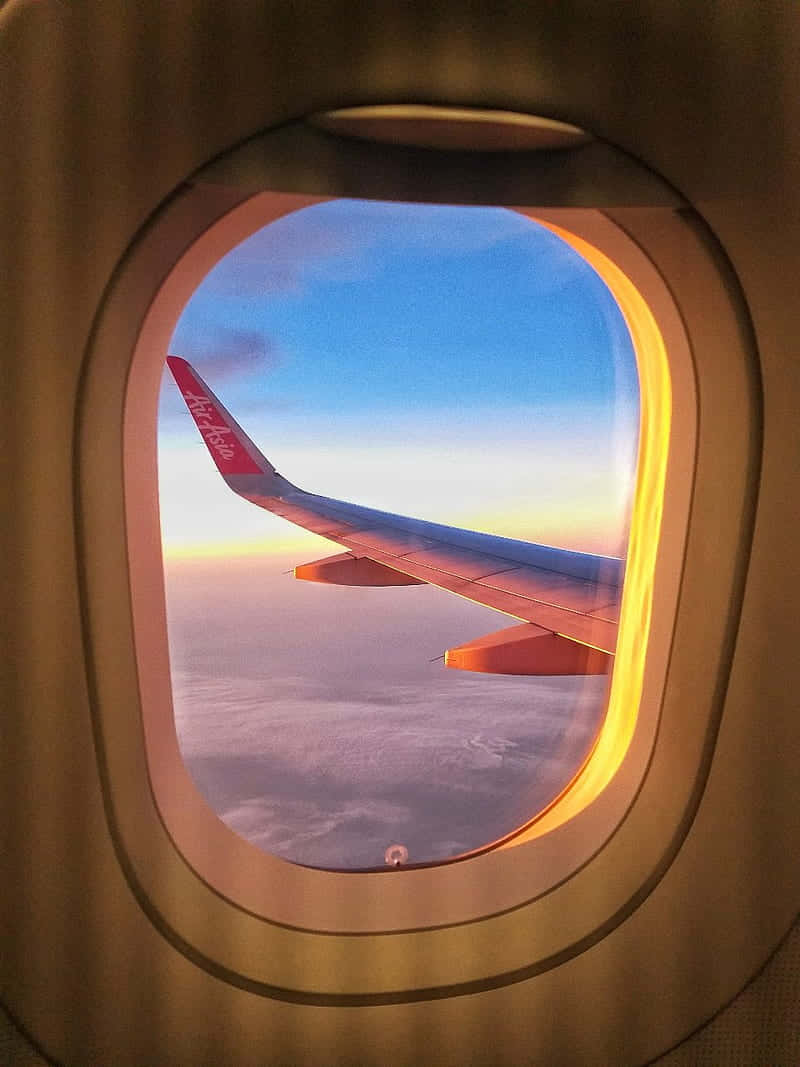 從飛機窗戶欣賞雲景 壁紙 — 帶有亞洲航空標誌的飛機機翼在透過飛機窗戶看到的日落天空中發光。