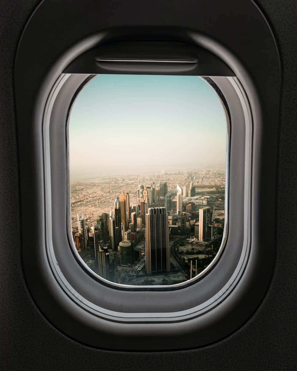 從飛機窗戶欣賞震撼美景 壁紙 — 透過飛機窗戶看到的現代城市天際線的空中景觀，帶有柔和的金色光線。