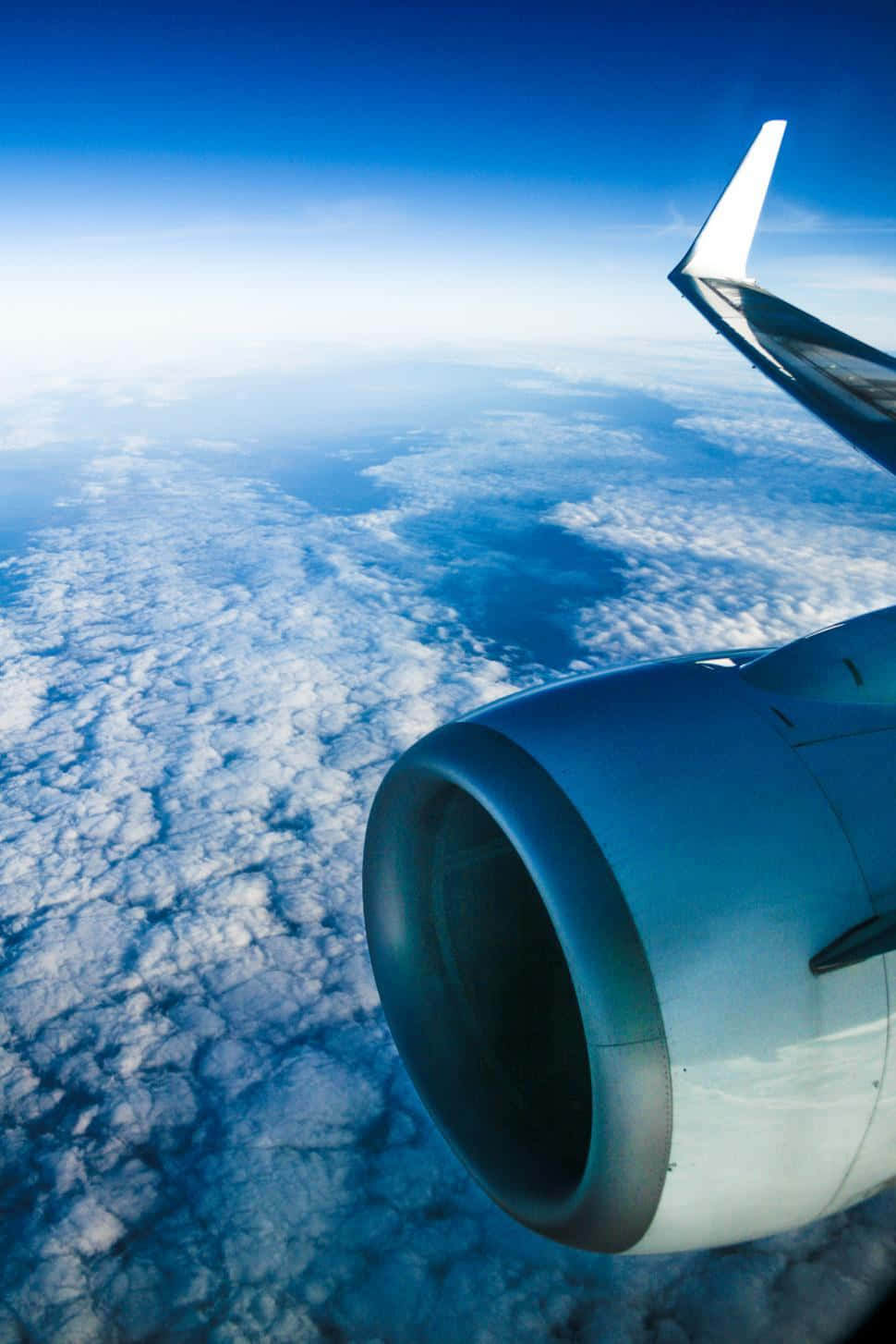 從飛機窗戶眺望地球 壁紙 — 從飛機窗戶俯瞰的空中視角，顯示噴射引擎和機翼在清澈天空下無盡的藍色雲層之上。