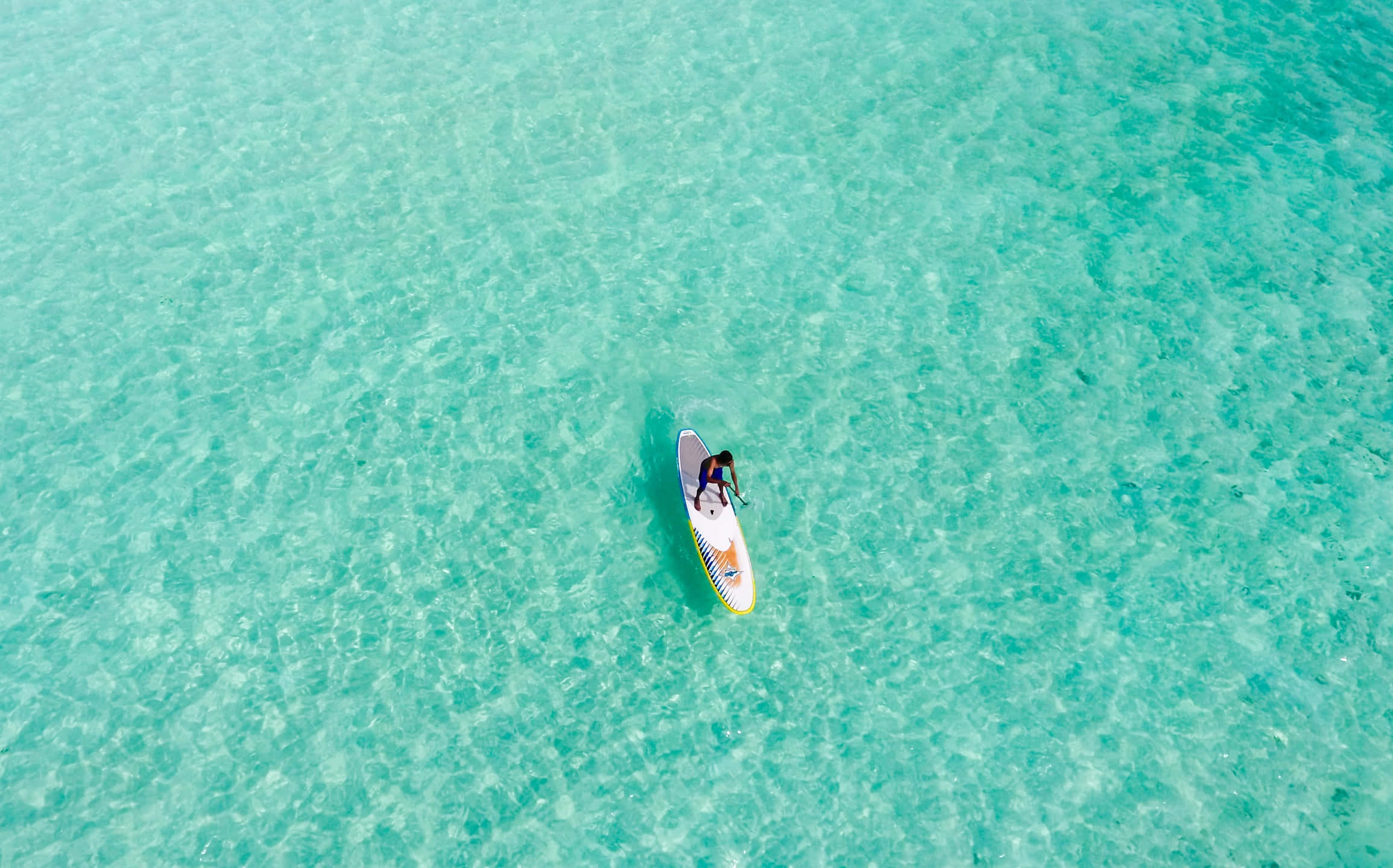 Paddleboarding 桌布 壁紙 — 從高空俯瞰，一名孤獨的槳板划手在清澈碧綠的水面上滑行。