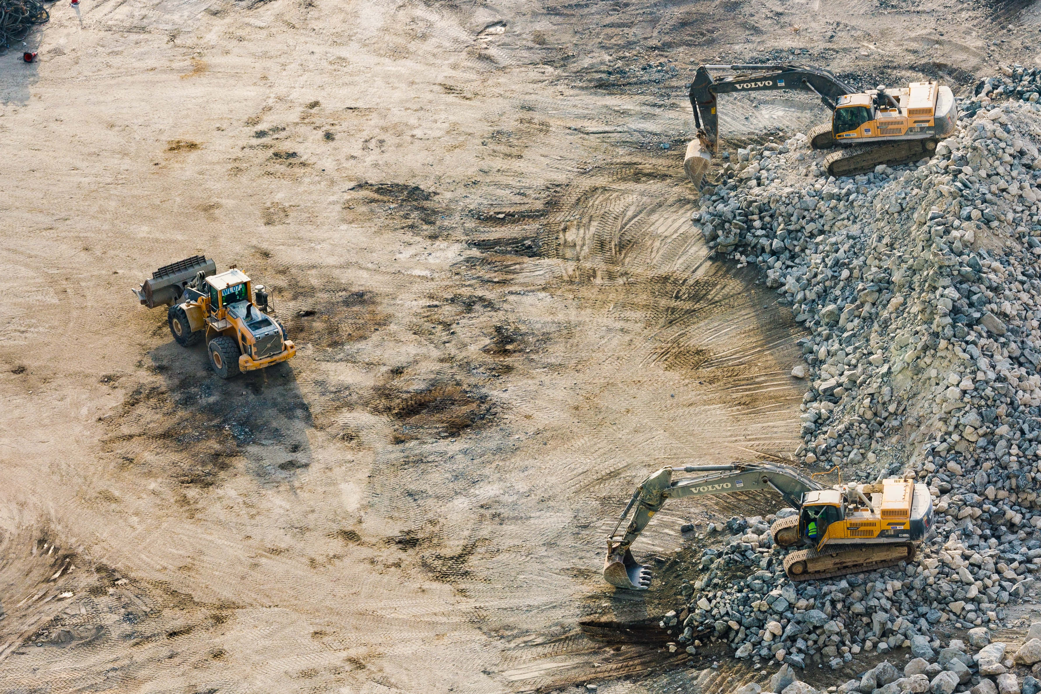 Mining 桌布 壁紙 — 從高空俯瞰，在明亮的日光下，岩石建築工地上有挖掘機和裝載機等重型機械在運作。