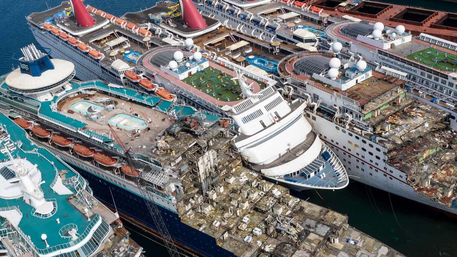 Cruise Ship 桌布 壁紙 — 從高空俯瞰，巨大的郵輪停泊在港口，其中一艘嚴重受損，甲板上散落著碎片。