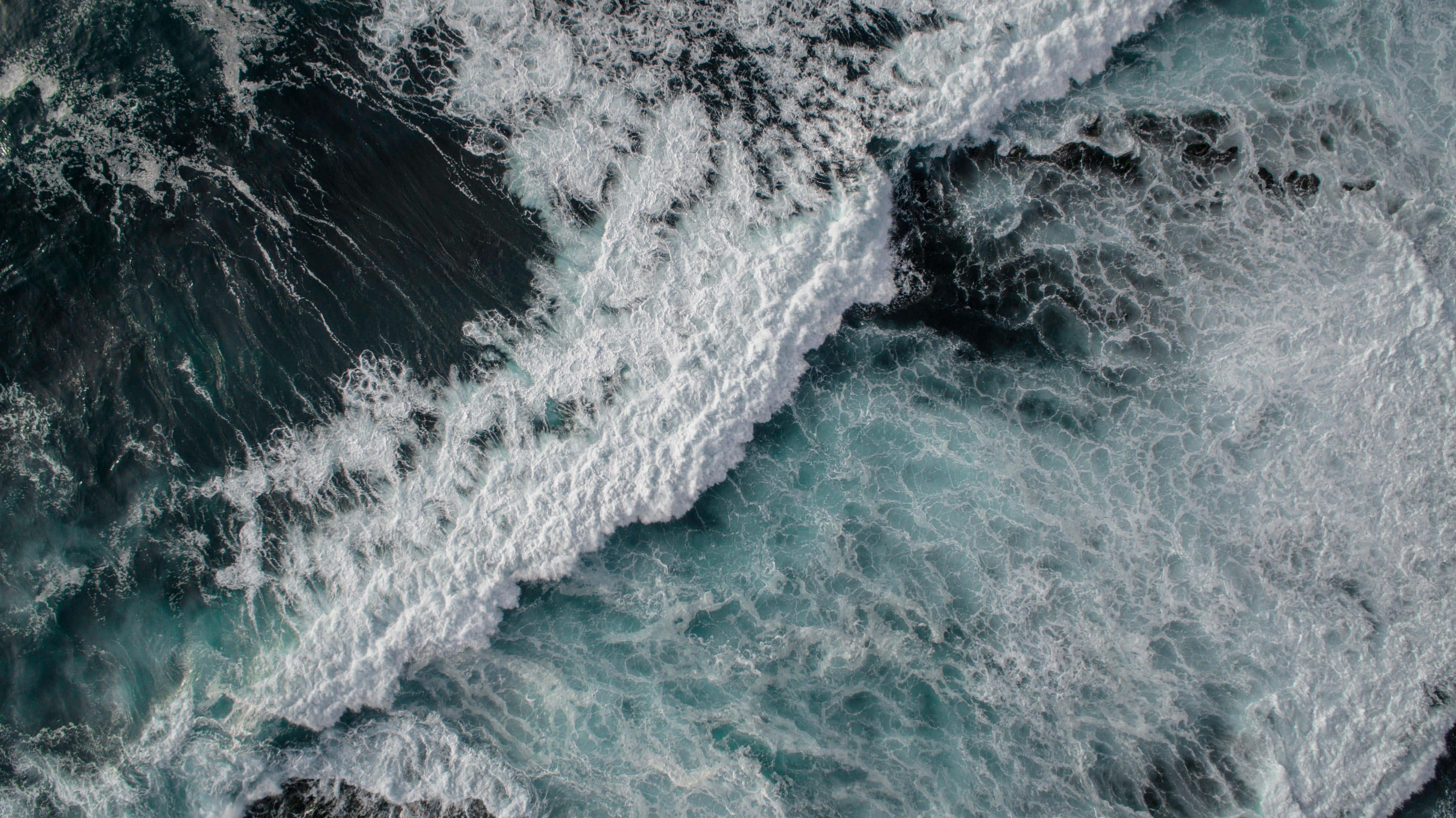 Tides 桌布 壁紙 — 從高空俯瞰，洶湧的海浪拍打著深藍綠色海水，激起白色泡沫。