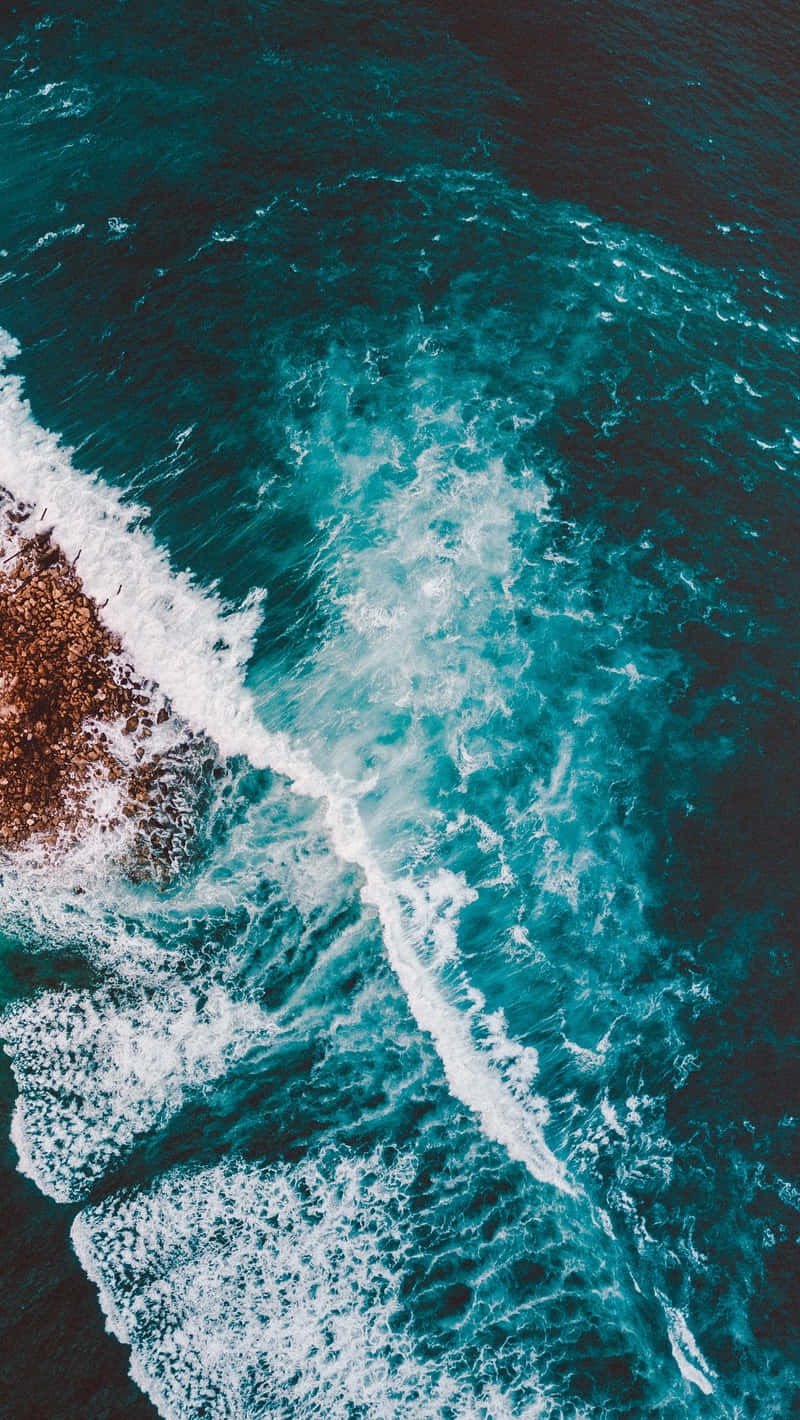 waves 桌布 壁紙 — 從高空俯瞰，碧綠色的海浪拍打著崎嶇的棕色岩石，激起白色泡沫。