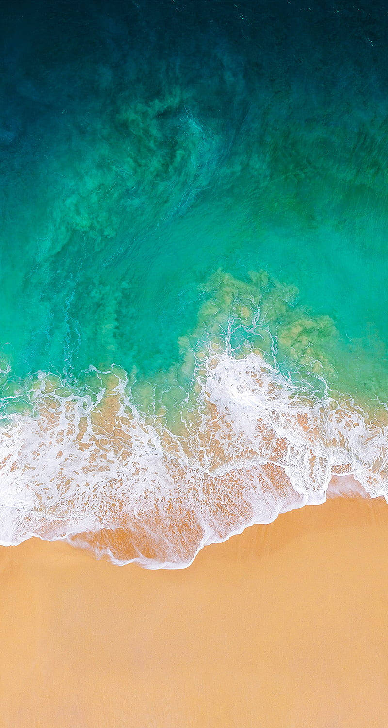 iPhone 桌布 壁紙 — 從高空俯瞰，碧綠色的海浪拍打著金色沙灘，形成漩渦狀的水紋。