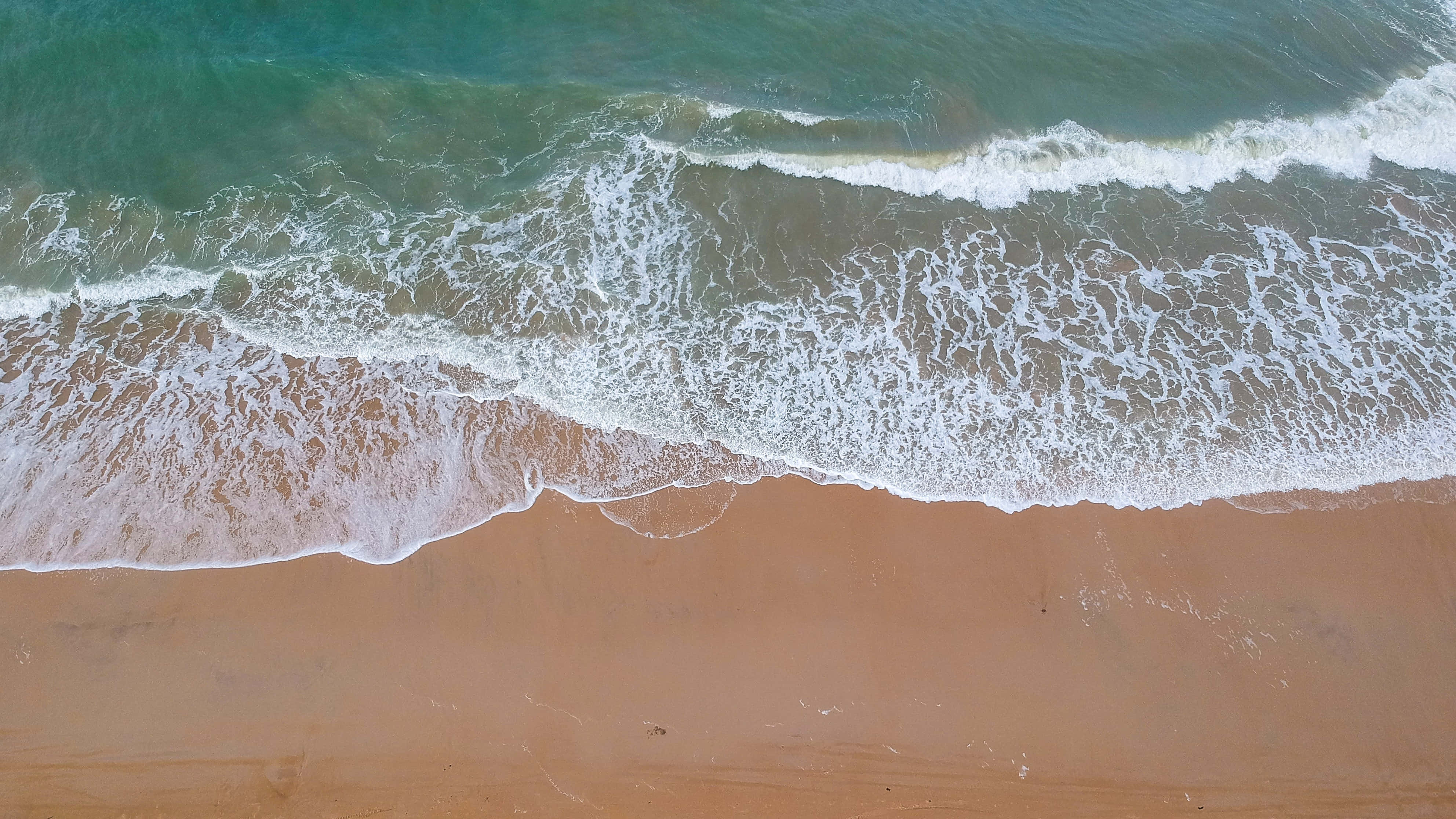 Beach Waves 桌布 壁紙 — 從高空俯瞰，碧綠色的海浪有節奏地拍打著金色沙灘，泛起白色泡沫。