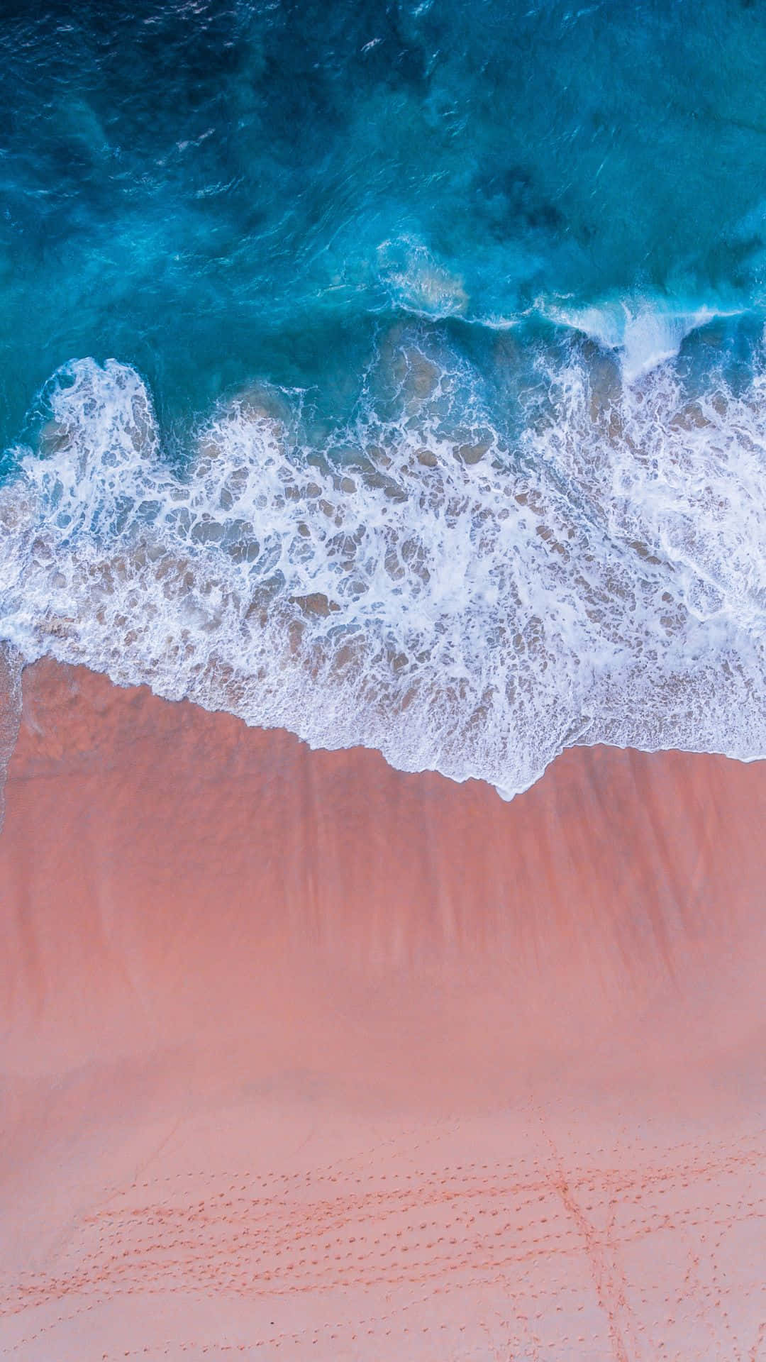 Pink Beach 桌布 壁紙 — 從高空俯瞰，綠松石色的海浪拍打著充滿活力的粉紅色沙灘，激起白色泡沫。