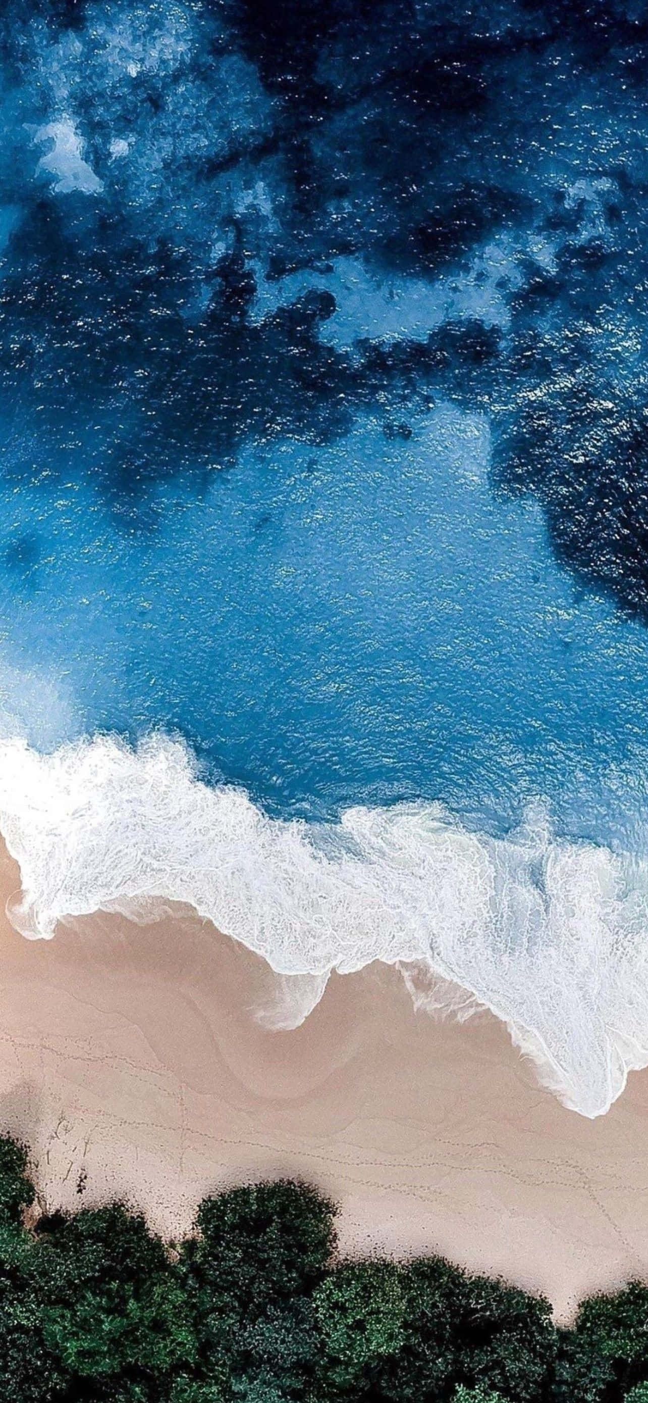 型格 iPhone 壁紙 桌布 壁紙 — 從高空俯瞰，綠松石色的海浪拍打著沙灘，沙灘邊緣長滿了茂密的綠色植物。