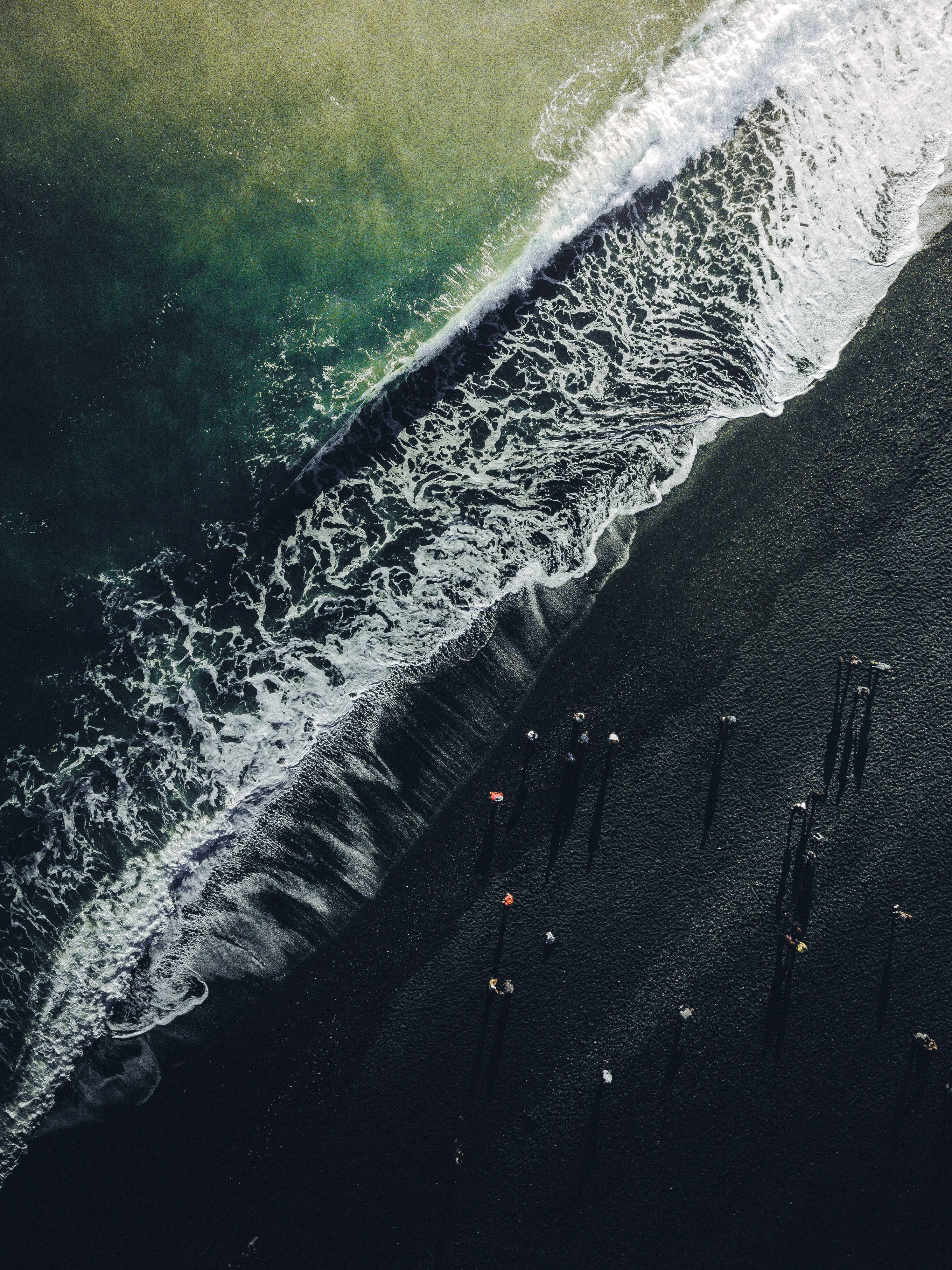 波浪 桌布 壁紙 — 從高空俯瞰，綠松石色的海浪拍打著漆黑的火山沙灘，沙灘上散落著微小的人影。