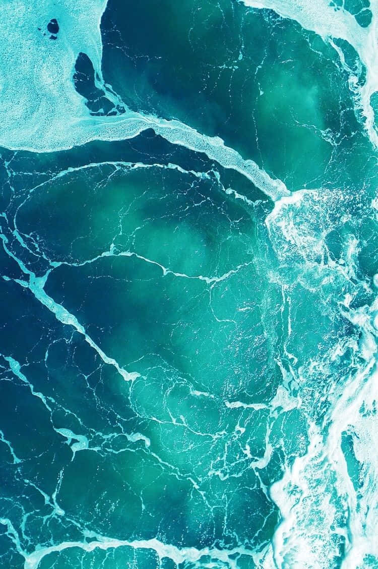 Seafoam Green 桌布 壁紙 — 從高空俯瞰，藍綠色海浪以複雜圖案旋轉，白色泡沫在深藍色海水上翻騰。