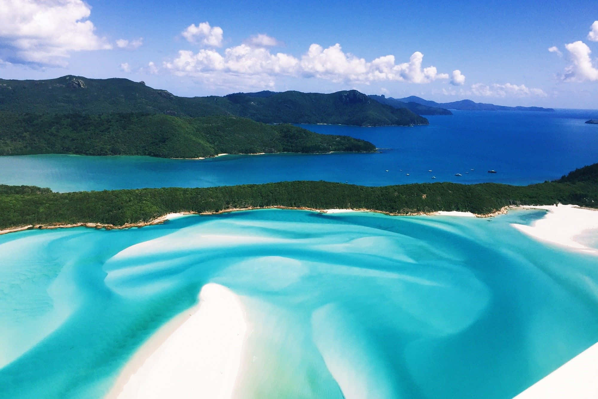 Australia Beach 桌布 壁紙 — 從高空俯瞰，迷人的藍綠色潟湖，白色沙洲蜿蜒穿過翠綠森林，上方是藍天白雲。