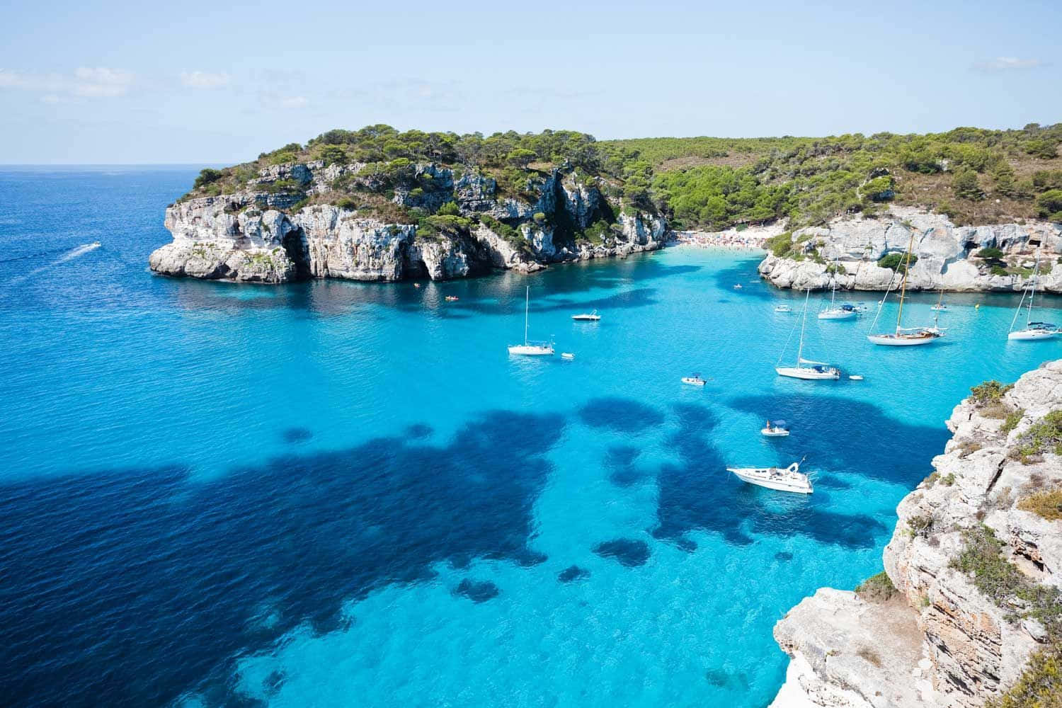 Spanish Beach 桌布 壁紙 — 從高空俯瞰一個令人驚嘆的碧綠海灣，白色帆船停泊在長滿綠植的岩石峭壁之間。