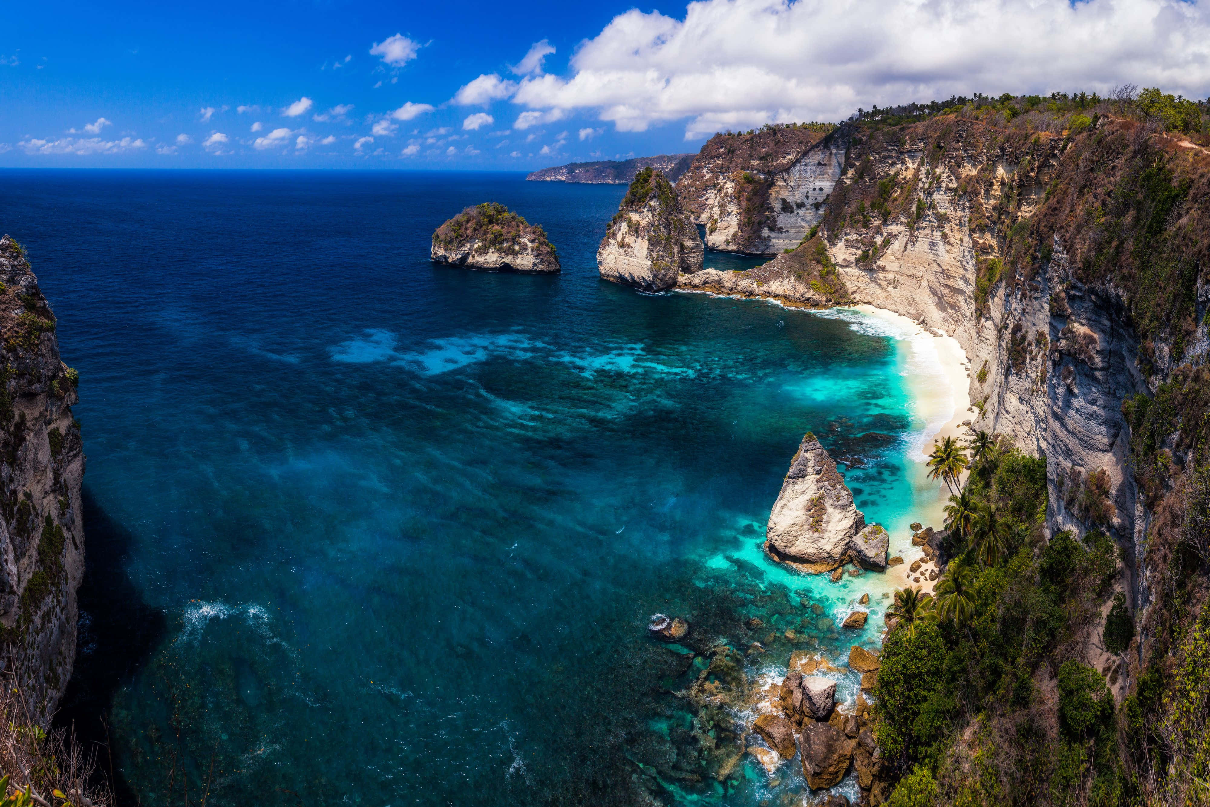 Bali Beach 桌布 壁紙 — 從高空俯瞰一個隱蔽的熱帶海灣，擁有碧綠色的海水、白色沙崖和茂密的綠色植物，在明亮的藍天下。