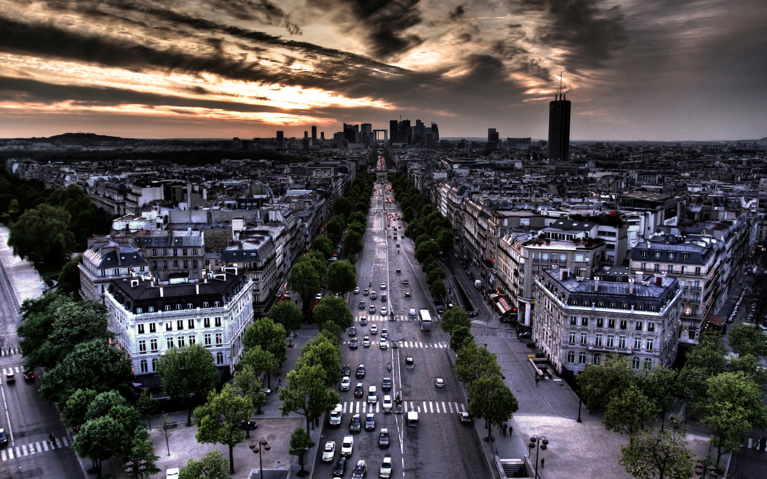 french 桌布 壁紙 — 從高空俯瞰一條宏偉的城市大道，兩旁種滿樹木和歷史建築，在戲劇性的日落天空下。
