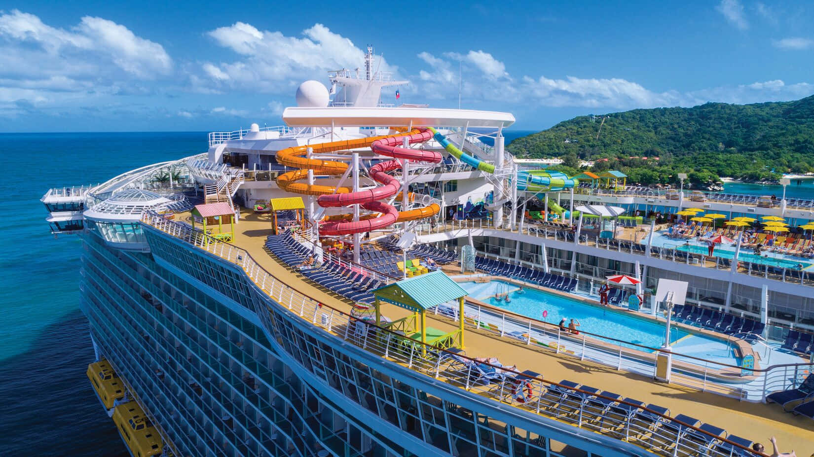 Cruise Ship 桌布 壁紙 — 從高空俯瞰一艘巨大的郵輪，擁有色彩繽紛的水滑梯、泳池和曬太陽的人們，背景是碧綠的海洋和綠色島嶼。