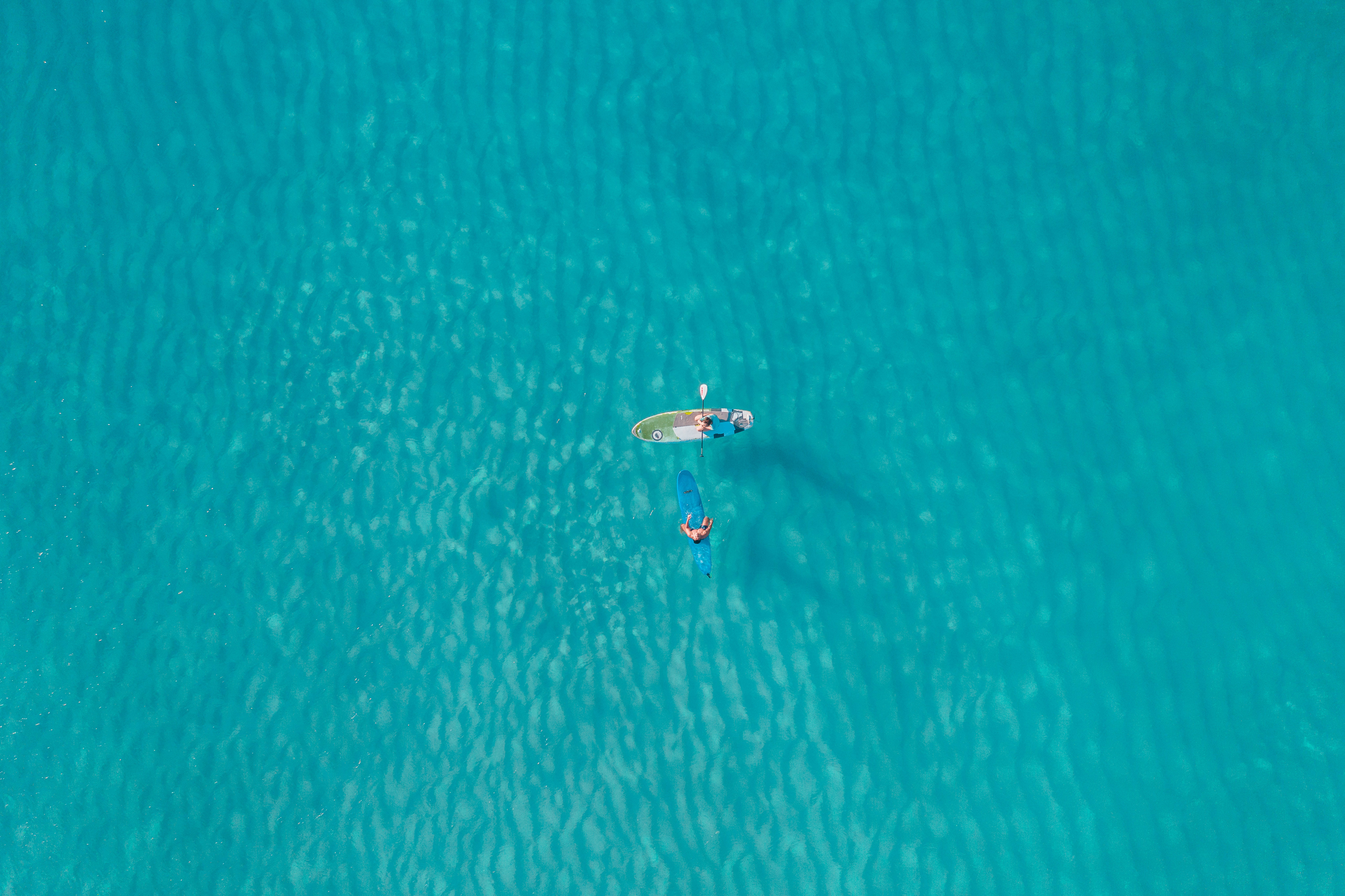 海洋 桌布 壁紙 — 從高空俯瞰兩人在平靜的藍綠色海水上划槳板的景象。