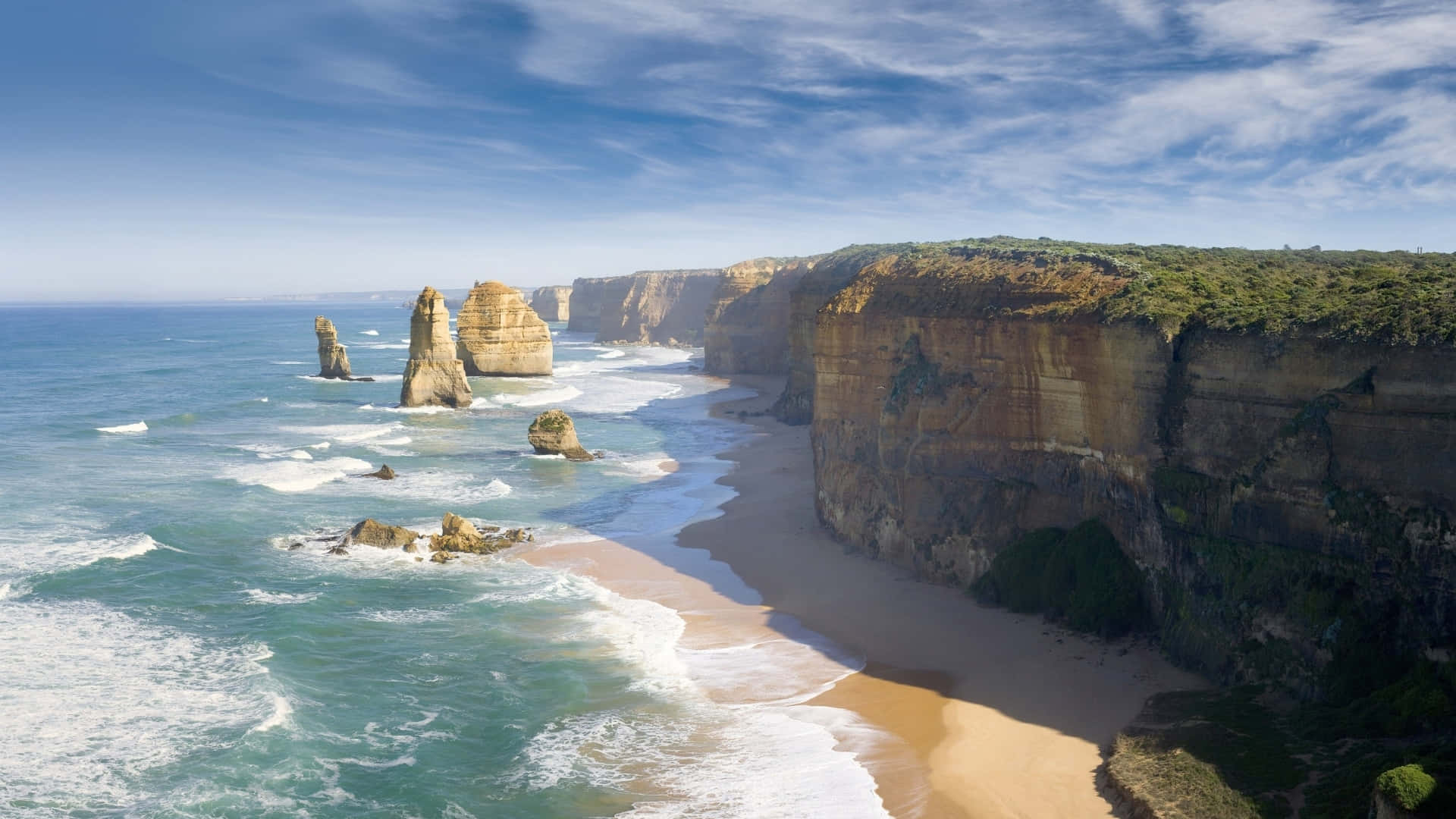 Australia 桌布 壁紙 — 從高空俯瞰十二門徒石灰岩柱從碧綠海水中聳立，旁邊是沙灘，上方是晴朗藍天與縷縷白雲。
