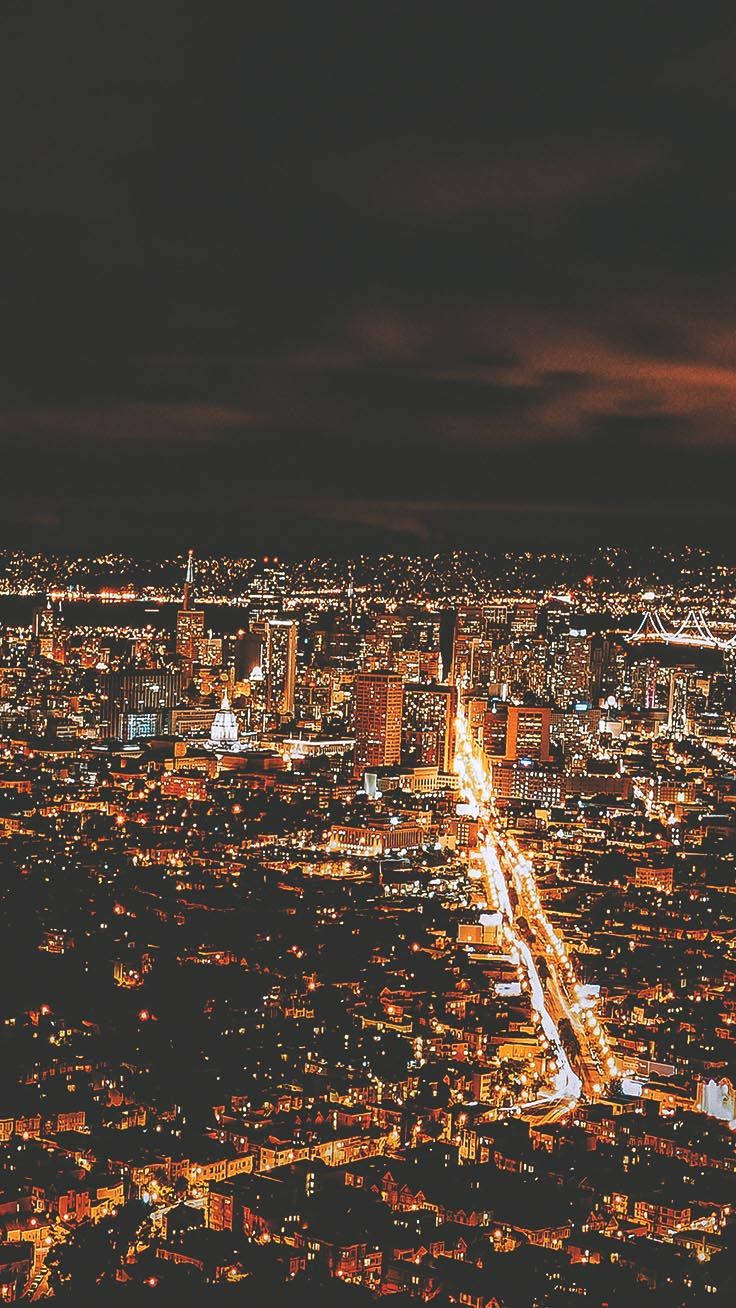 San Francisco Phone 桌布 壁紙 — 從高空俯瞰夜晚中燈火通明的街道和建築物，在陰暗多雲的天空下延伸的城市景觀。