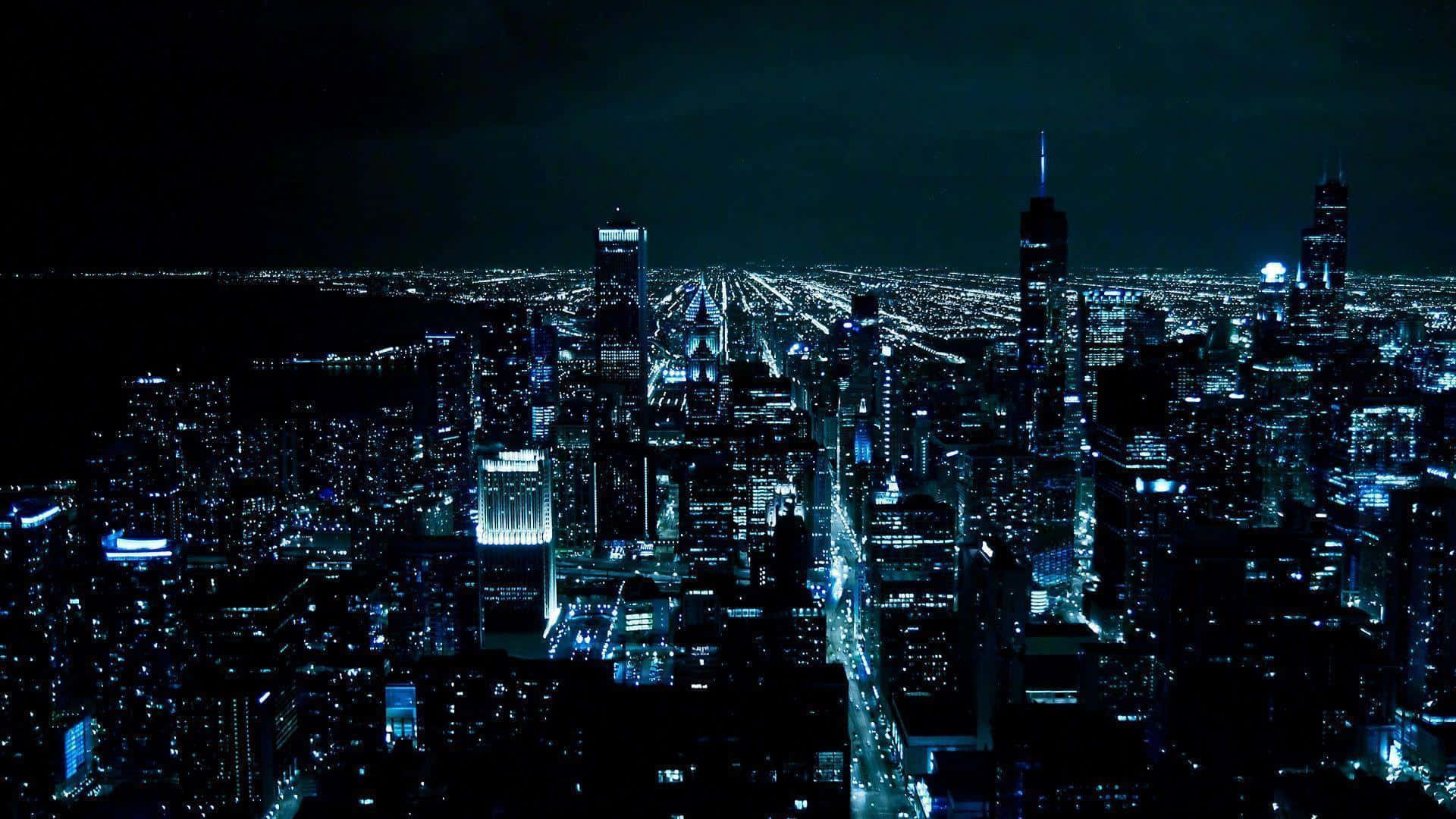 Gotham City 桌布 壁紙 — 從高空俯瞰夜晚的城市景觀，廣闊的城市被冷色調的藍色和白色燈光照亮，襯托著黑暗的天空。
