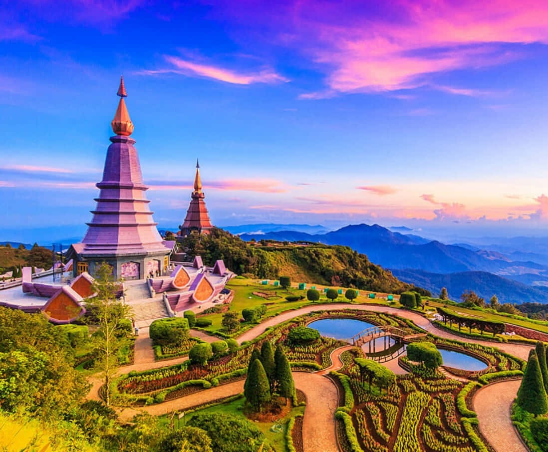 Asia 桌布 壁紙 — 從高空俯瞰山頂上充滿活力的寺廟建築群，精心修剪的花園蜿蜒穿過茂密的綠植，背景是戲劇性的粉紅和藍色日落天空。