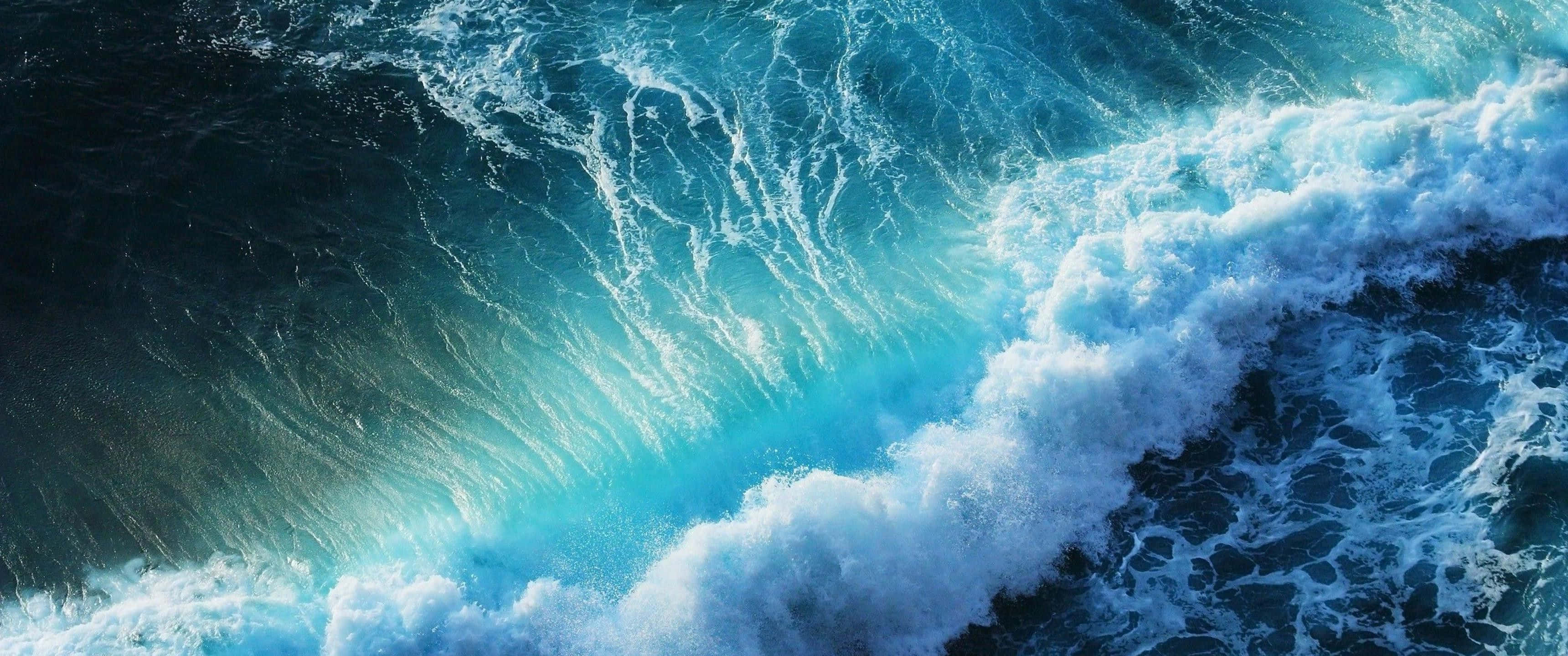 wide 桌布 壁紙 — 從高空俯瞰巨大海浪撞擊深藍色海水，激起藍綠色泡沫的景象。
