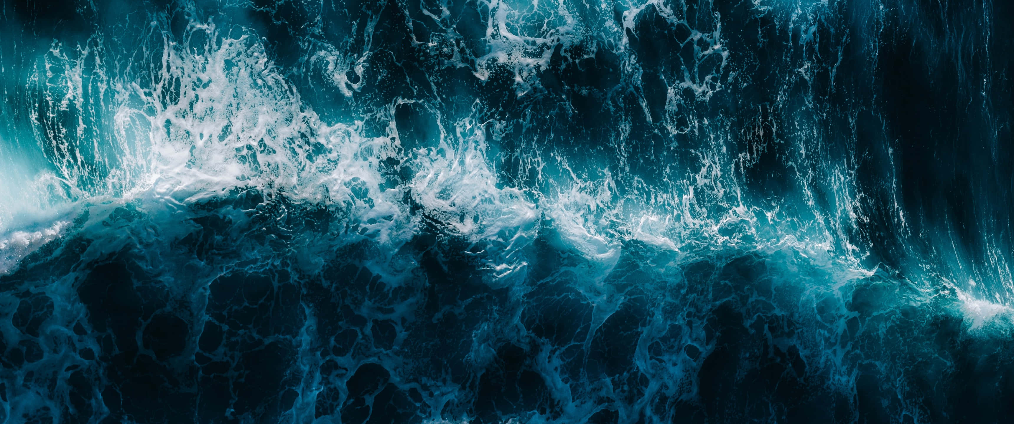 waves 桌布 壁紙 — 從高空俯瞰的海洋波浪撞擊景象，呈現深藍綠色海水和泡沫般的白色浪花。