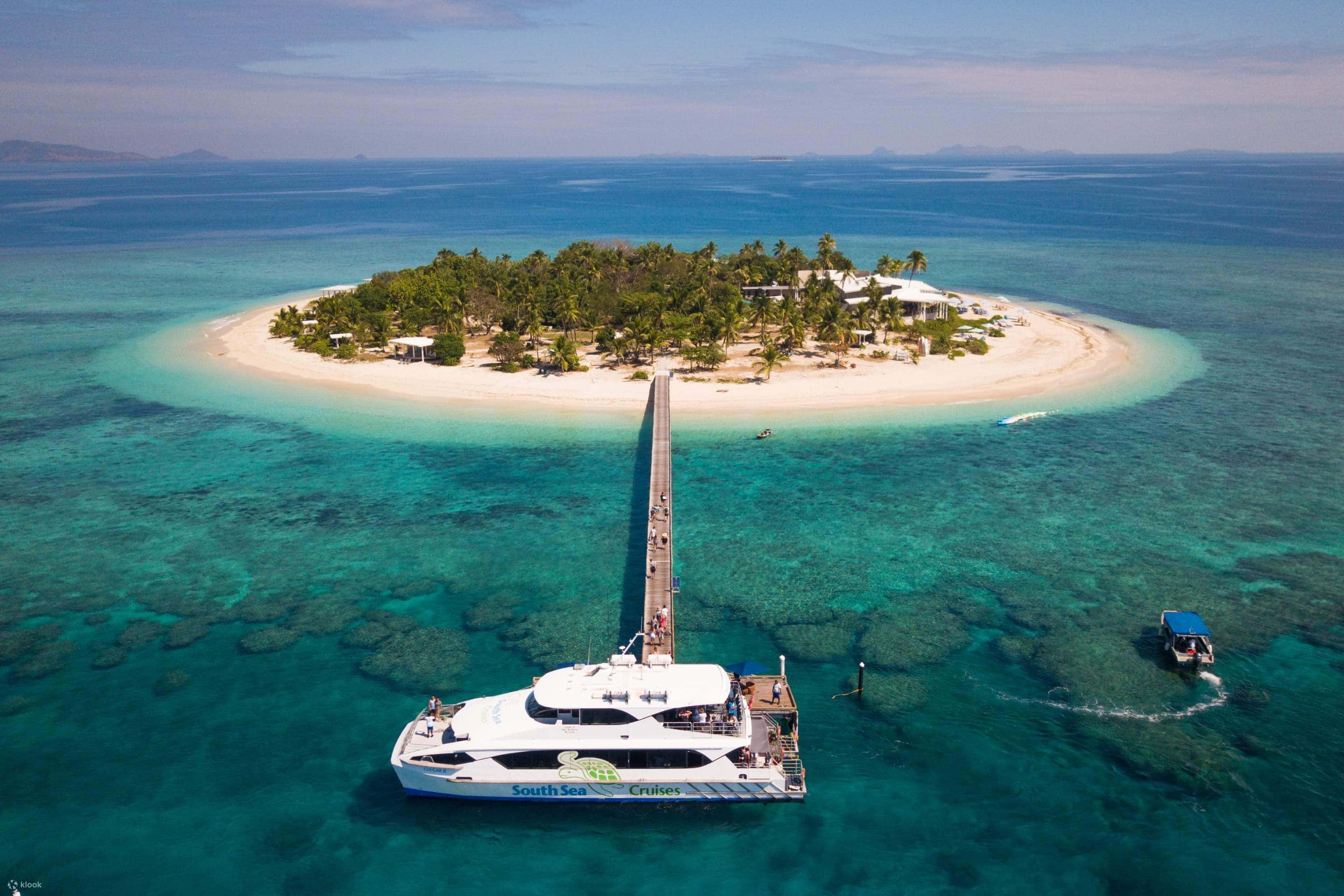 Fiji Beach 桌布 壁紙 — 從高空俯瞰純淨熱帶島嶼，碧綠海水與停泊在長碼頭的雙體船。