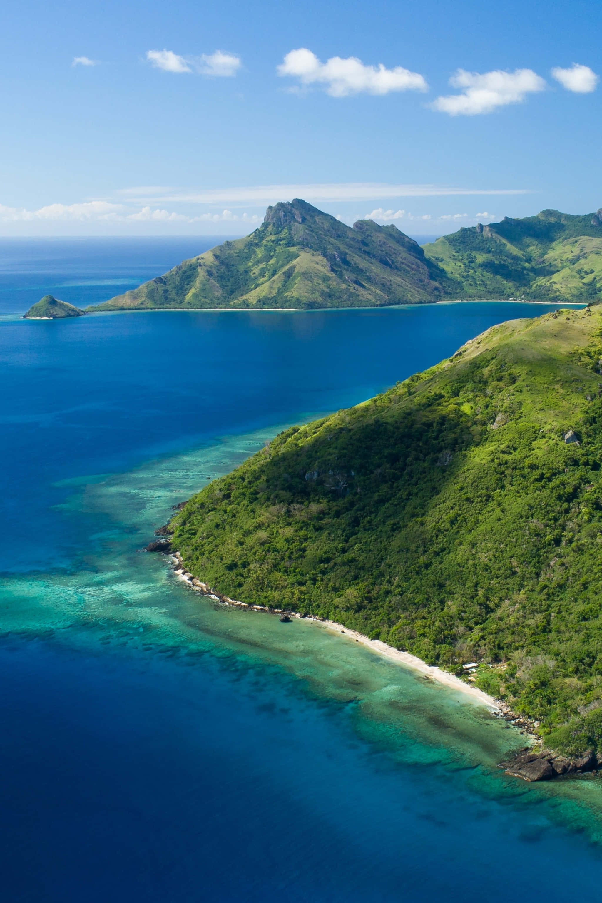Fiji Beach 桌布 壁紙 — 從高空俯瞰翠綠島嶼，擁有碧綠潟湖和深藍海洋，天空明亮。