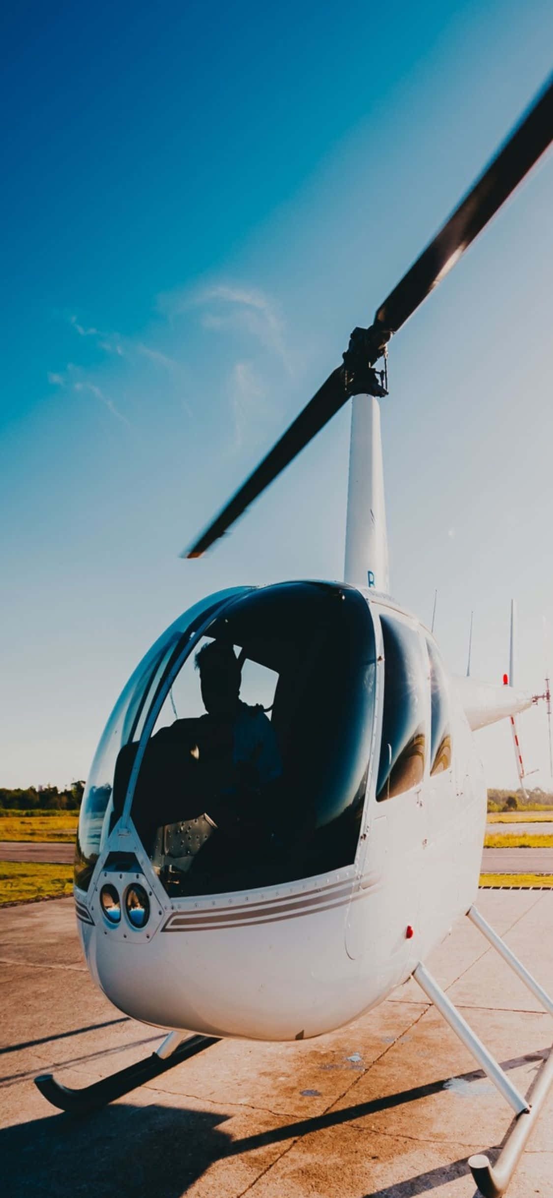 從高空俯瞰自然之美 壁紙 — 一架流線型白色直升機停在停機坪上，天空清澈湛藍，柔和陽光投下長長的影子。