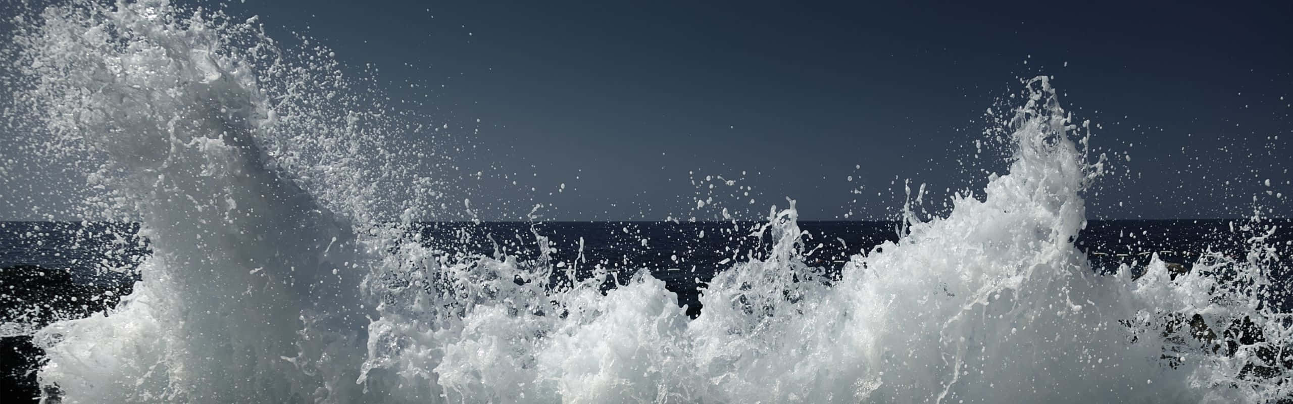 海浪衝擊，白色飛沫映襯著深藍色的海洋和天空。