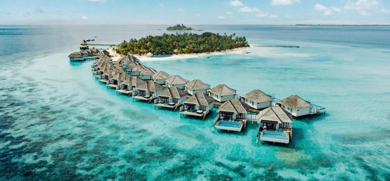 Maldives Island 桌布 壁紙 — 從鬱蔥的熱帶島嶼延伸至碧綠海洋水面的茅草屋頂水上平房的鳥瞰圖。