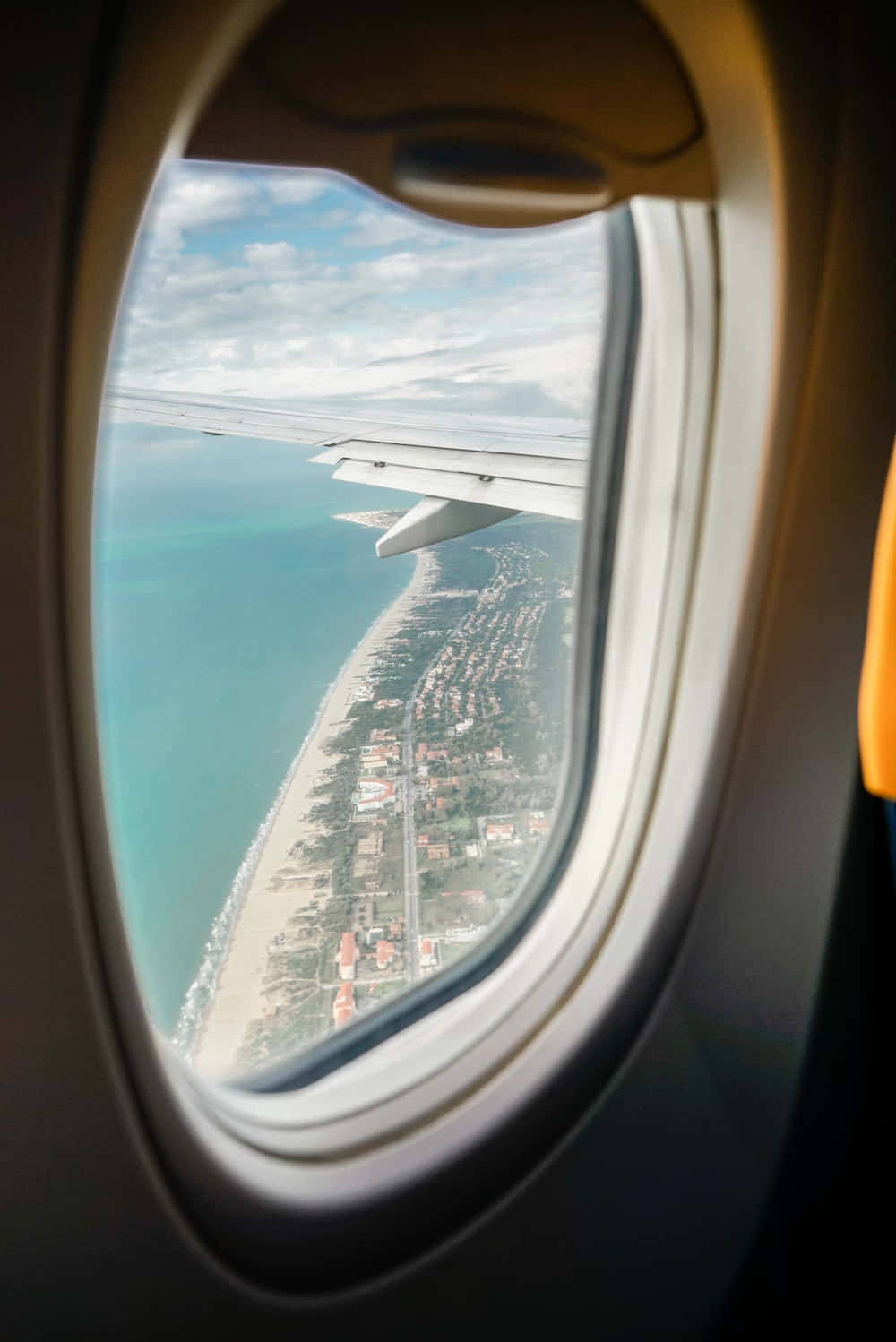 從鳥瞰視角起飛 壁紙 — 從飛機窗戶俯瞰，機翼下方是碧綠的海洋和沿海小鎮。