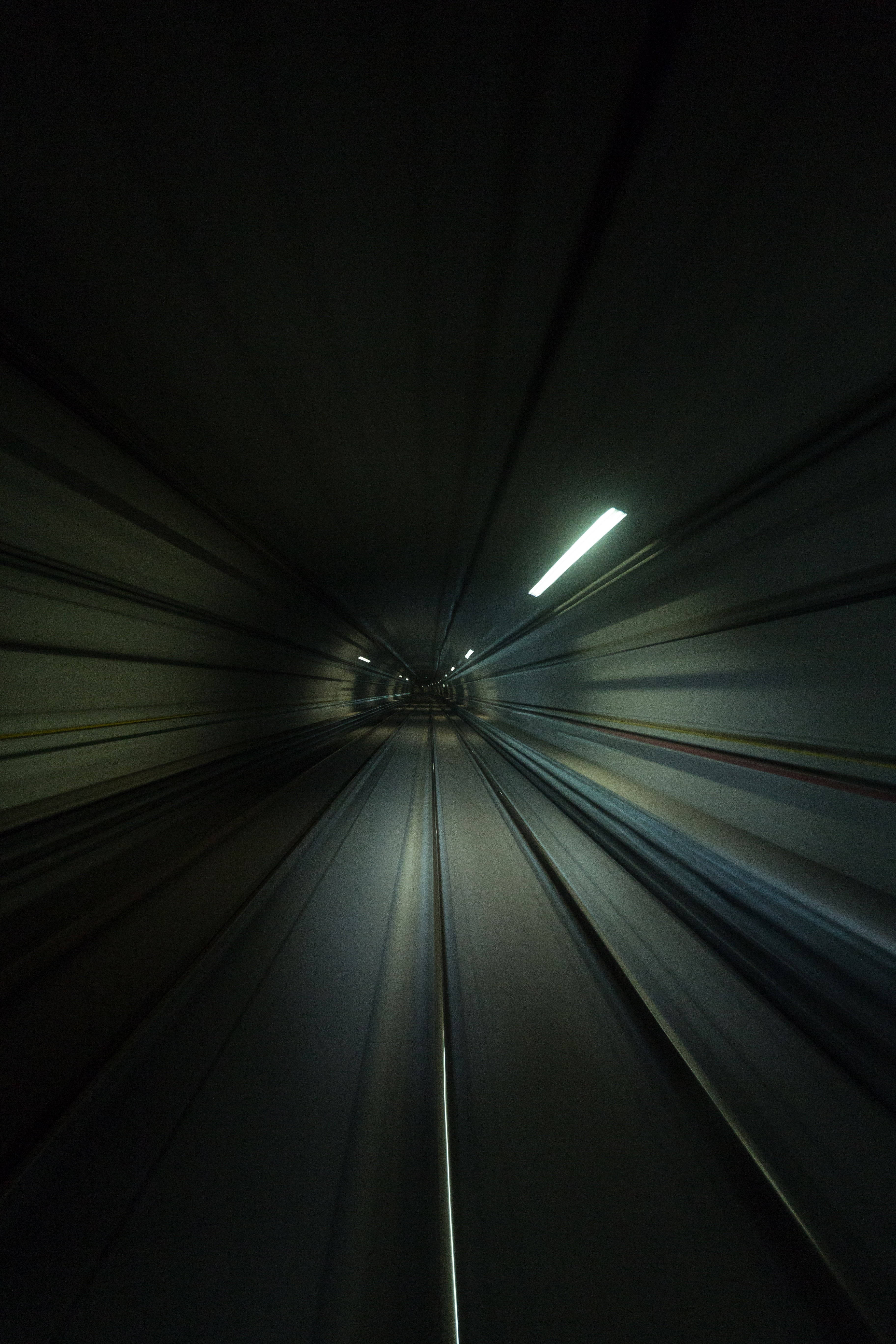 train tunnel 桌布 壁紙 — 從黑暗隧道內部拍攝的高速動態模糊照片，光線和鐵軌匯聚向遠處的出口。