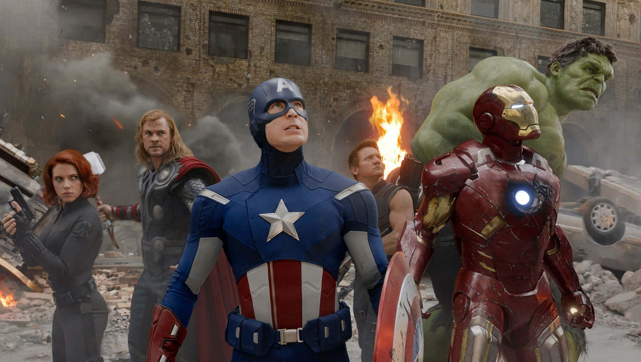 Superhero Movies 桌布 壁紙 — 復仇者聯盟在煙霧瀰漫的城市戰場集結，美國隊長領軍，鐵甲奇俠發光，變形俠醫聳立，雷神揮動他的錘子。