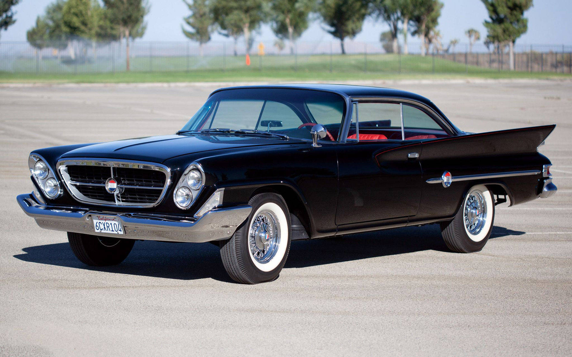 復古 Chrysler 車款 壁紙 — 一架時尚的黑色1950年代經典汽車，配備白色側壁輪胎和鍍鉻細節，在明亮的日光下停泊在瀝青停車場上。