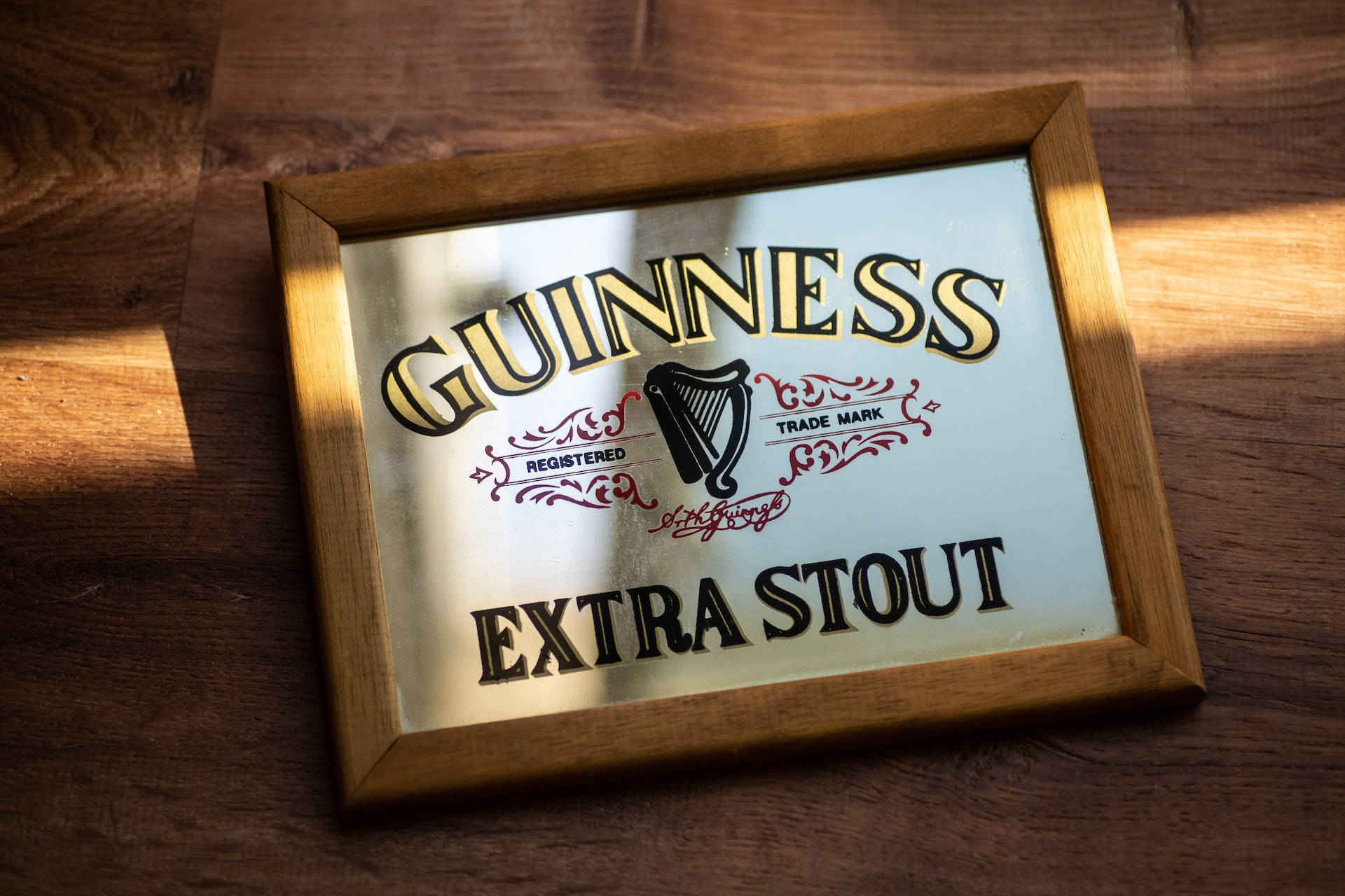 帶框的健力士Extra Stout鏡面標誌在木桌上，有陽光。