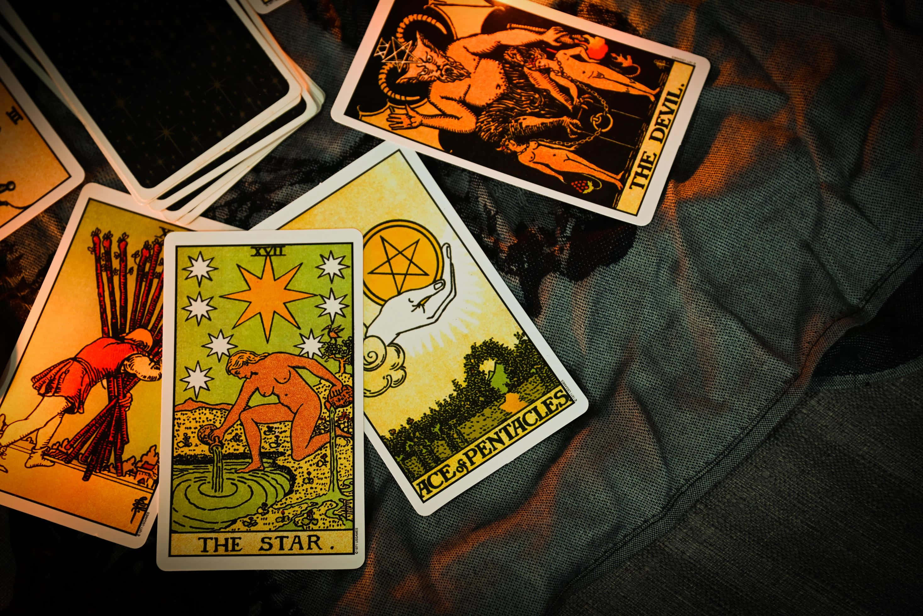 塔羅牌 桌布 壁紙 — 復古塔羅牌，包括星星、惡魔和錢幣王牌，在溫暖燈光下放置於深色紋理布料上。
