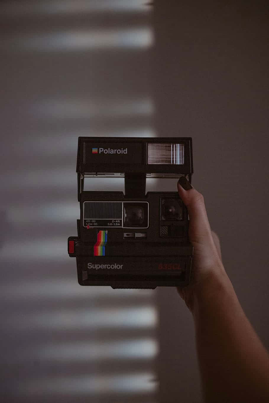 手拿著黑色Polaroid Supercolor相機，後面牆上有光條。