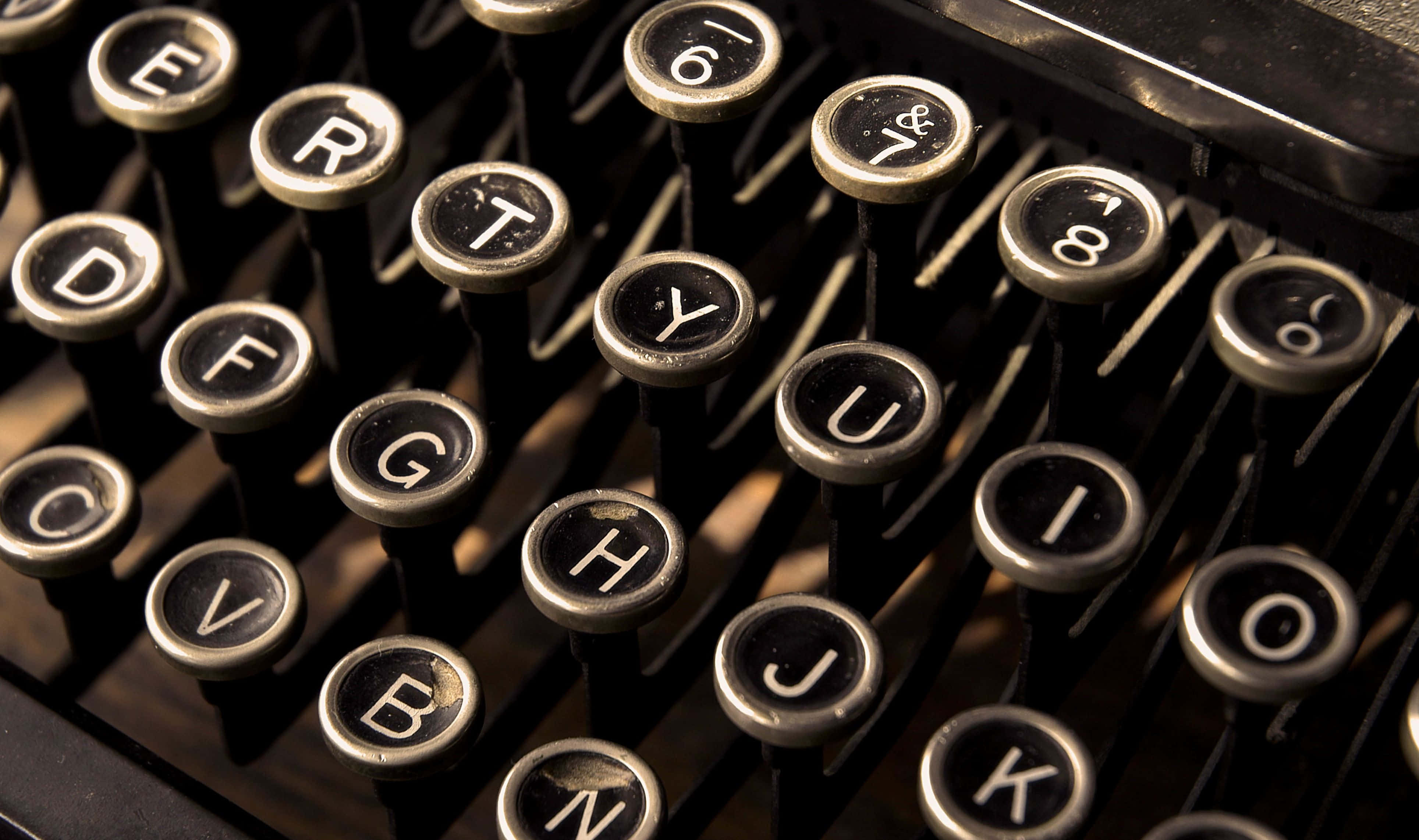 Journalism 桌布 壁紙 — 復古打字機按鍵特寫，磨損的銀色字體在溫暖金色光線下。