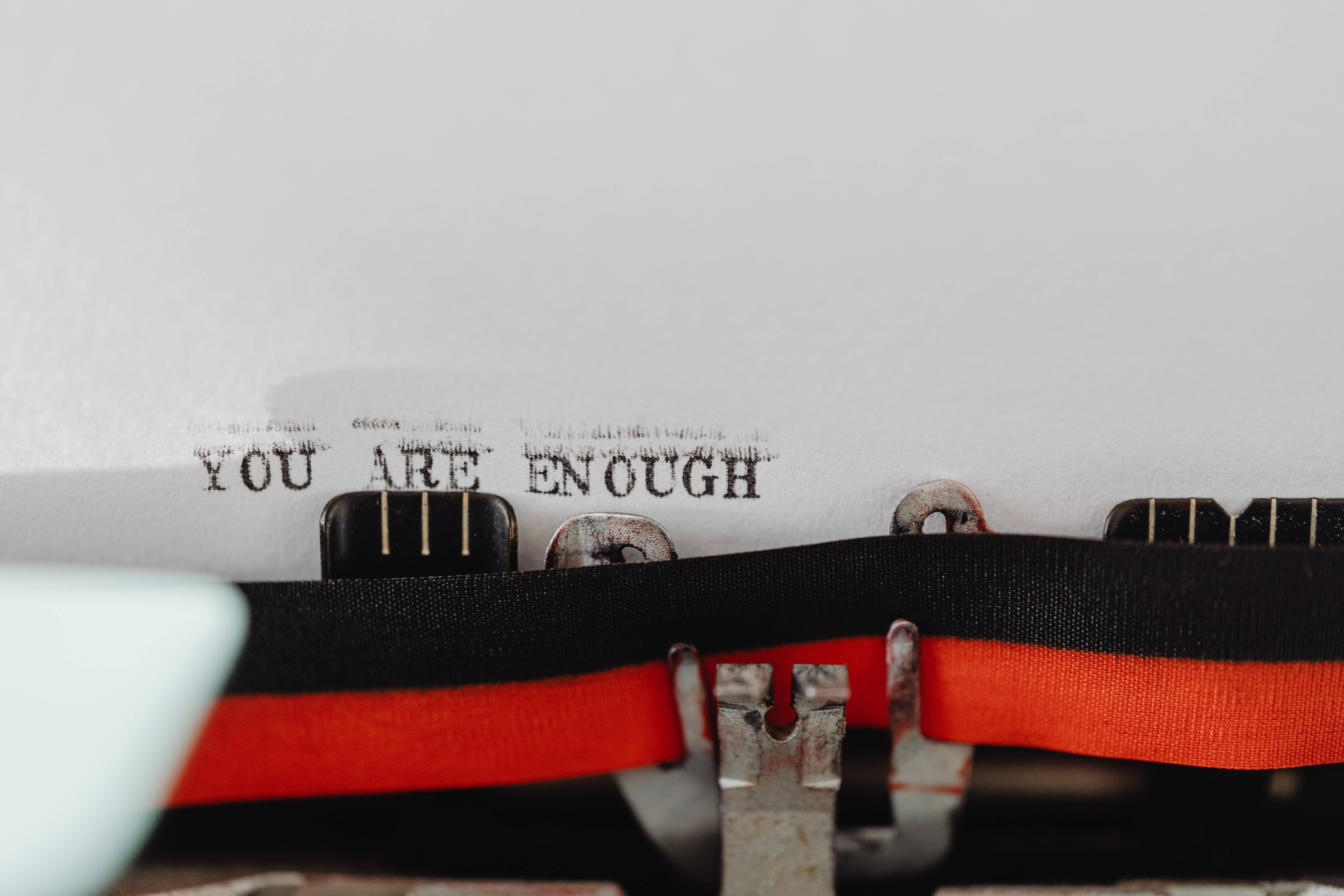 勵志語錄 桌布 壁紙 — 復古打字機的特寫，白色紙上打有「YOU ARE ENOUGH」字樣，並以紅色絲帶點綴。