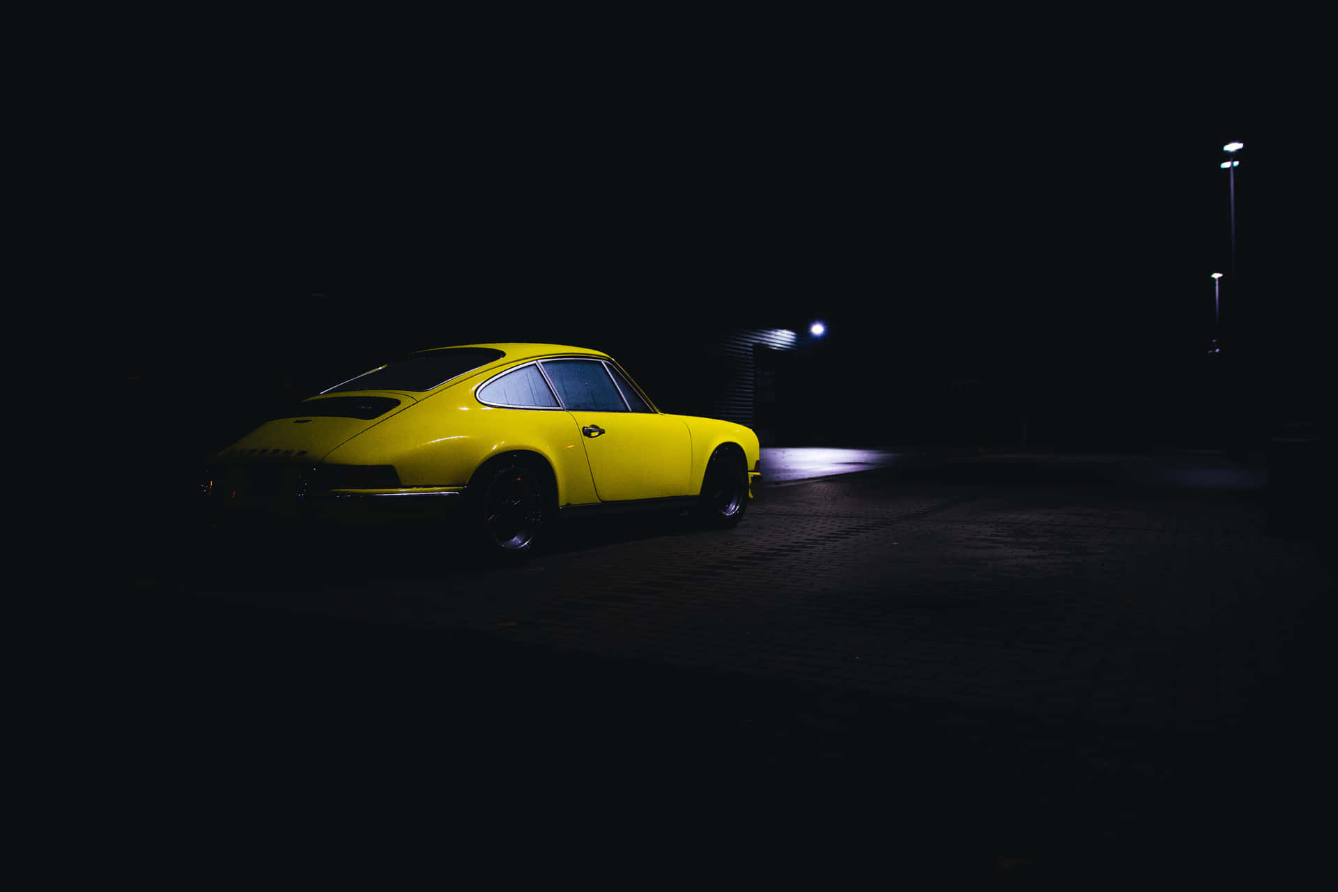 一輛明亮的黃色復古跑車在夜間停放在黑暗的磚路上，在單一路燈下。