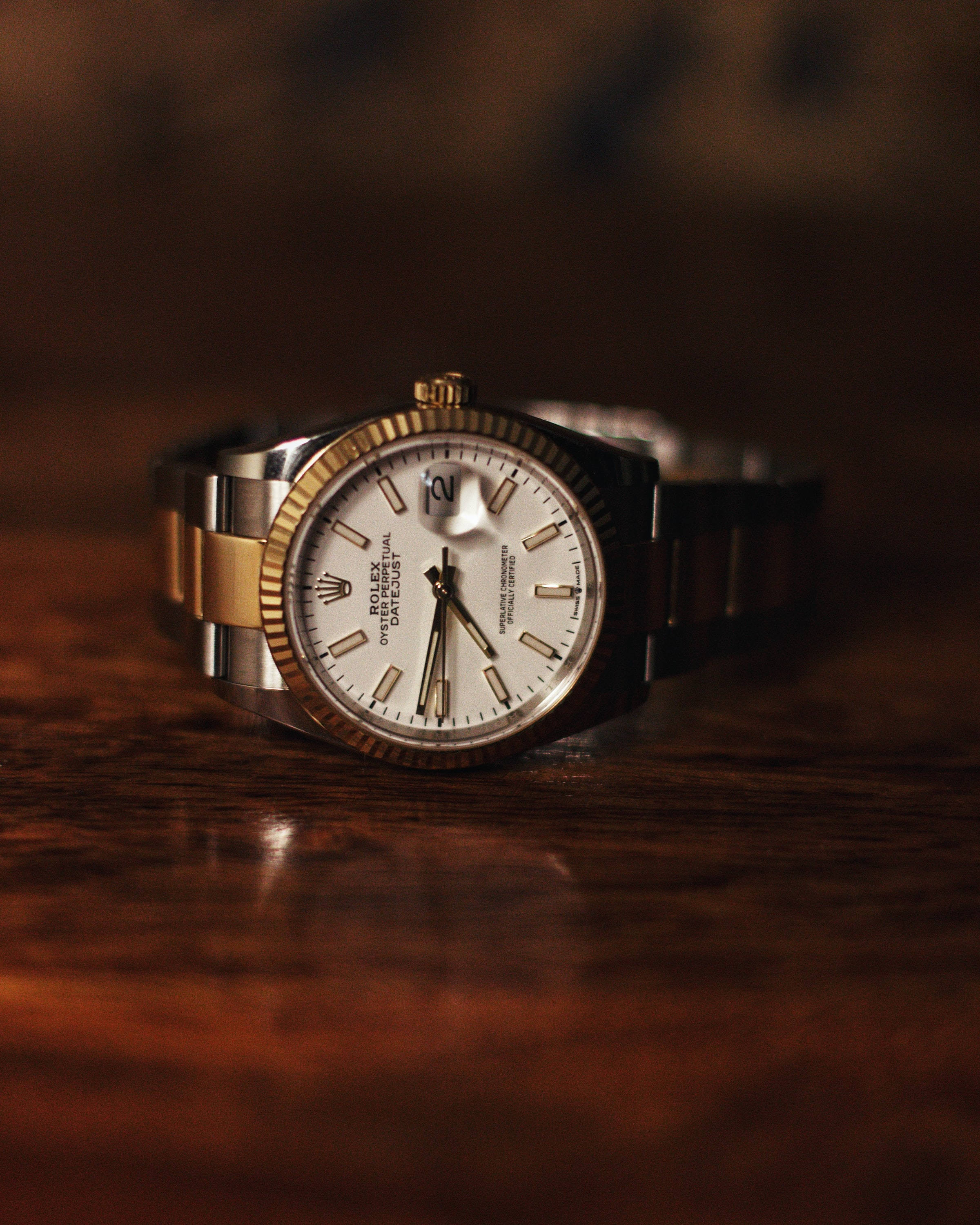 復古木質羅夏 壁紙 — 一款豪華的勞力士 Oyster Perpetual Datejust 手錶，配備金鋼錶帶，在溫暖的環境燈光下優雅地放置在豐富的木質表面上。