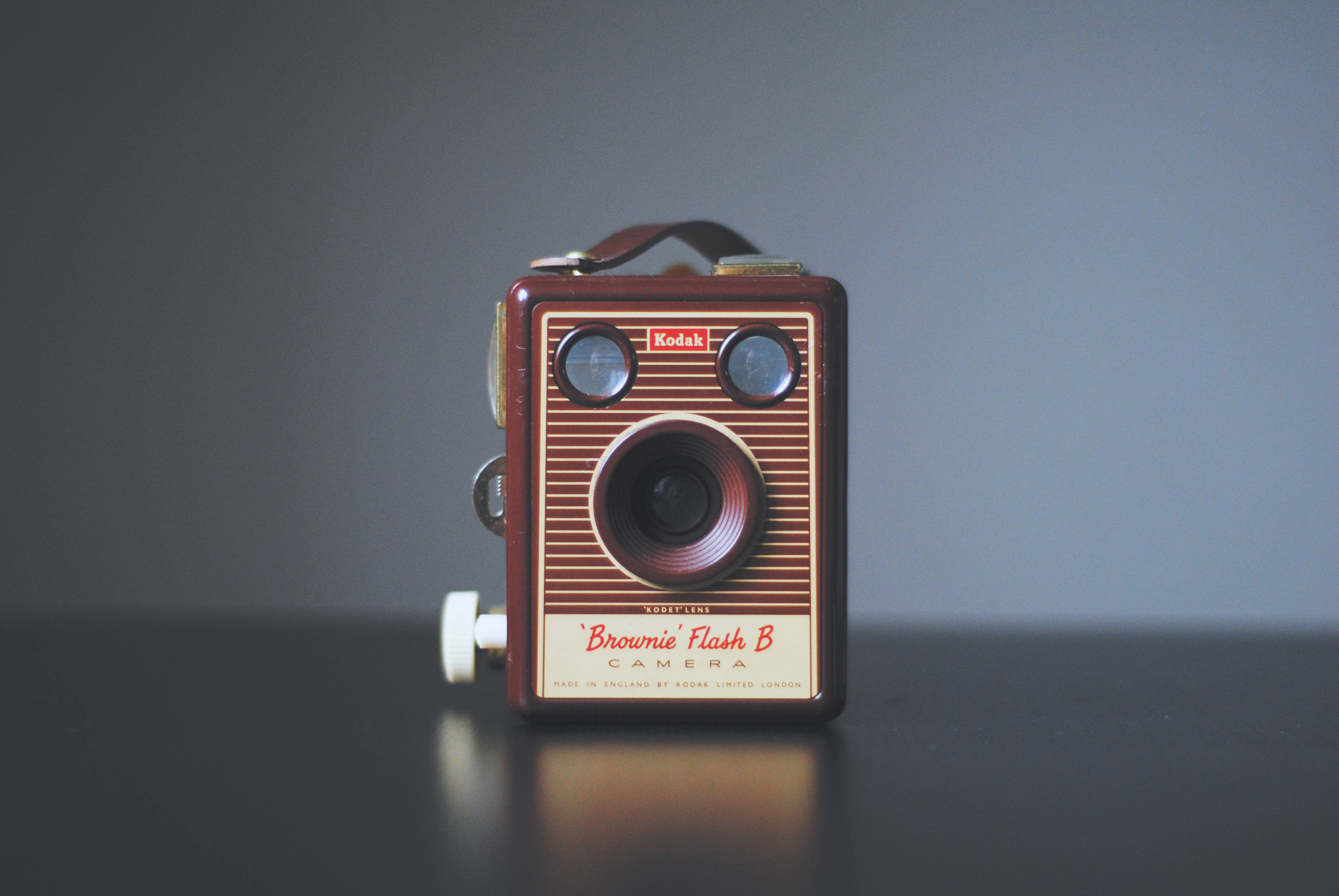 復古極簡棕色相機 壁紙 — 一部復古棕色Kodak Brownie Flash B相機居中放置在深色反光表面上，背景為柔和的灰色。