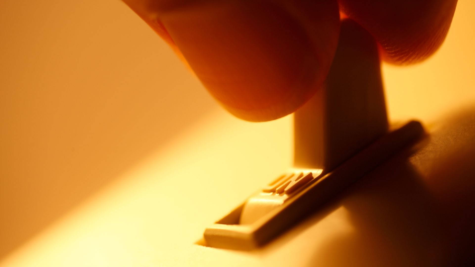 復古燈開關 黃色燈光 壁紙 — 手指在溫暖金色燈光下按下電燈開關的特寫，投射出柔和陰影。