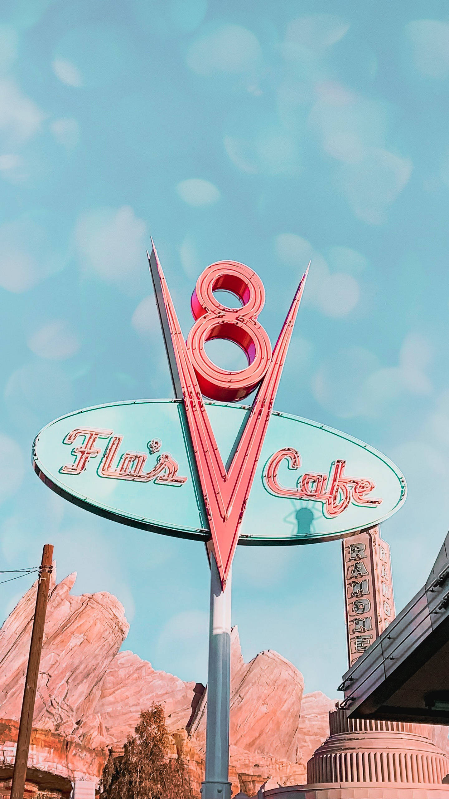 迪士尼 桌布 壁紙 — 復古粉紅色霓虹燈招牌，為 Flair's Cafe 設計，形狀像一個風格化的數字八，背景是明亮的藍天，帶有散景效果。