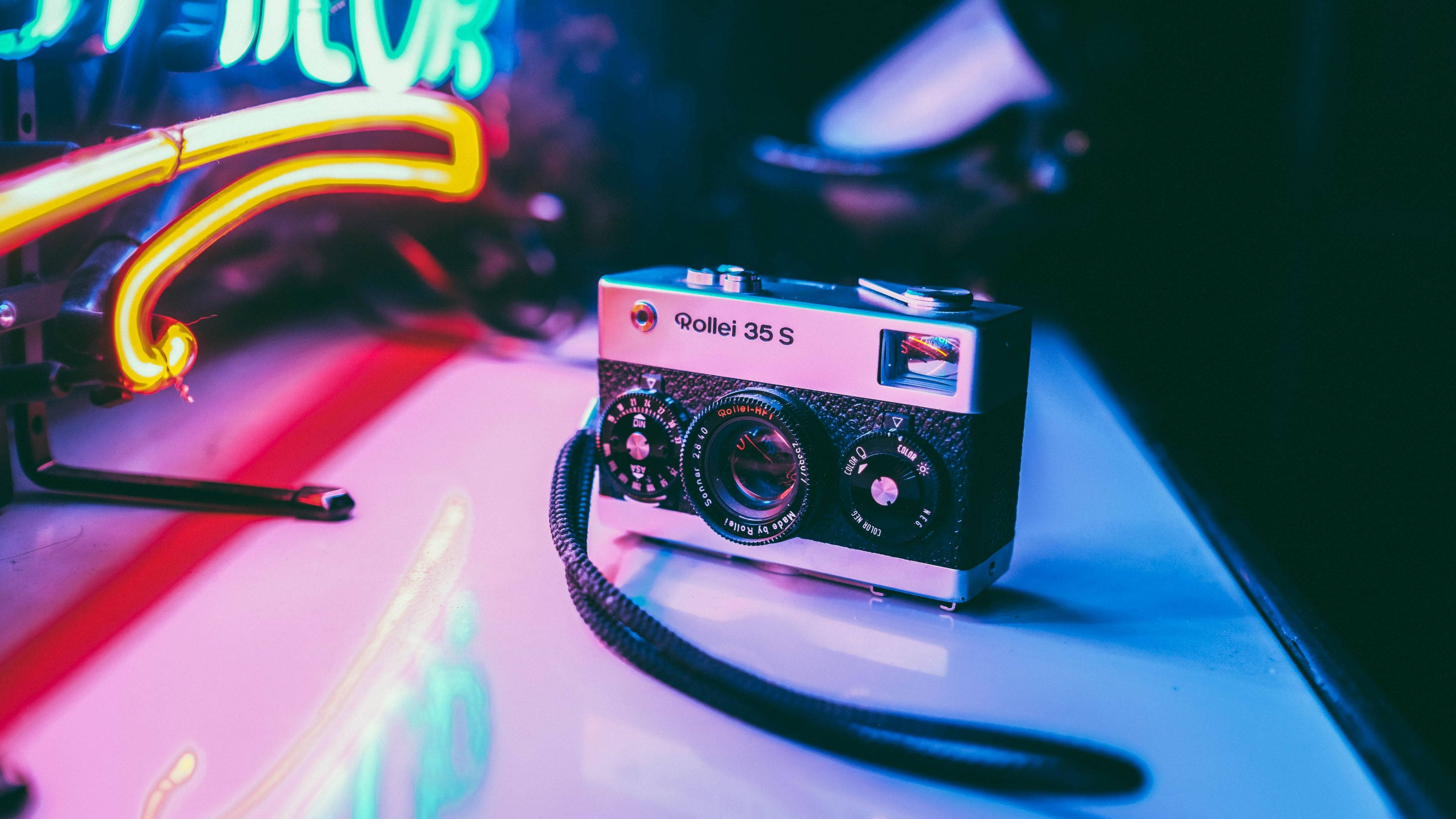 復古美學羅萊爾膠片相機 壁紙 — 一部復古 Rollei 35 S 相機放置在光滑表面上，沐浴在充滿活力的霓虹燈光中，投射出色彩繽紛的倒影。