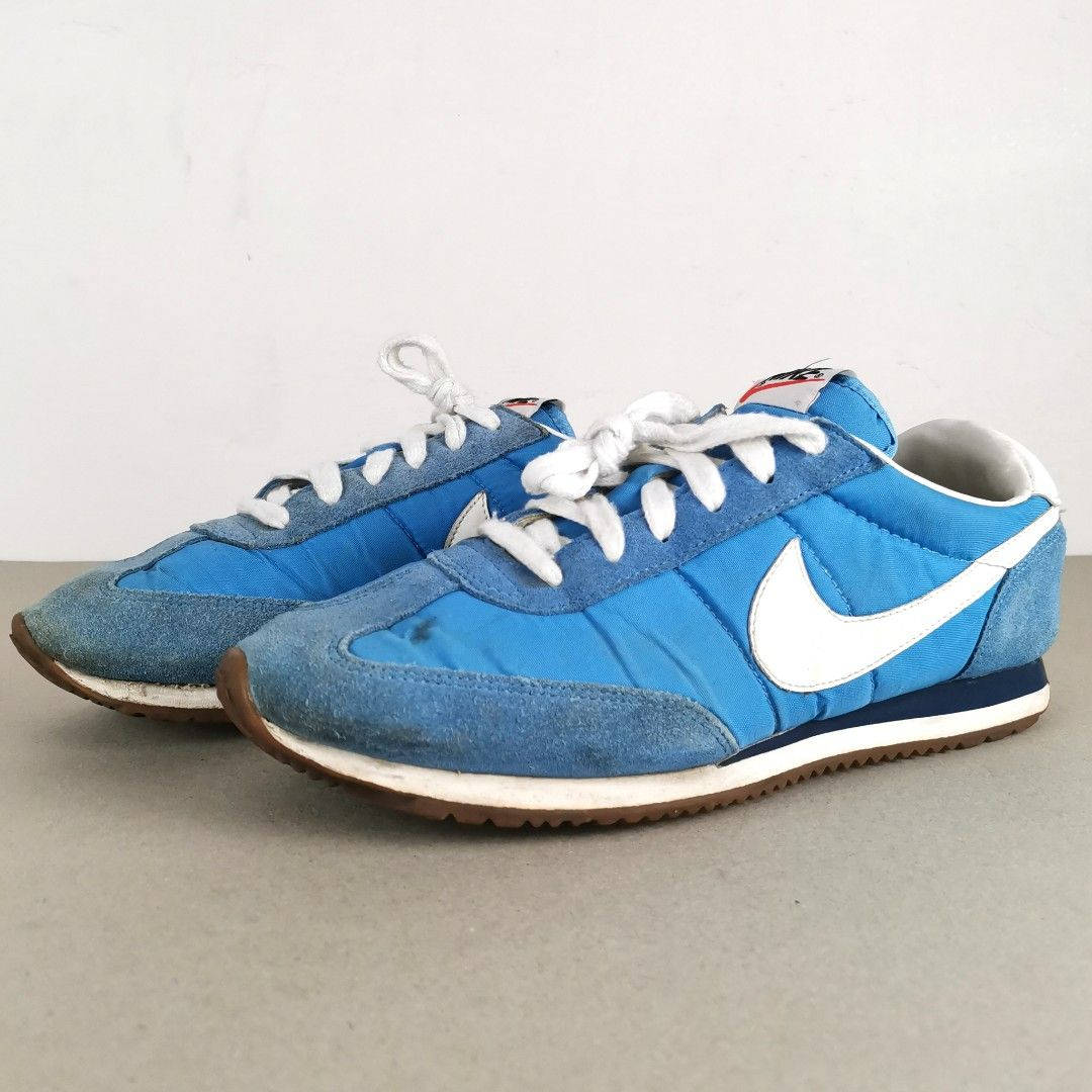 穿過的藍色Nike運動鞋，配有白色鞋帶和Swoosh標誌，放在灰色表面上。