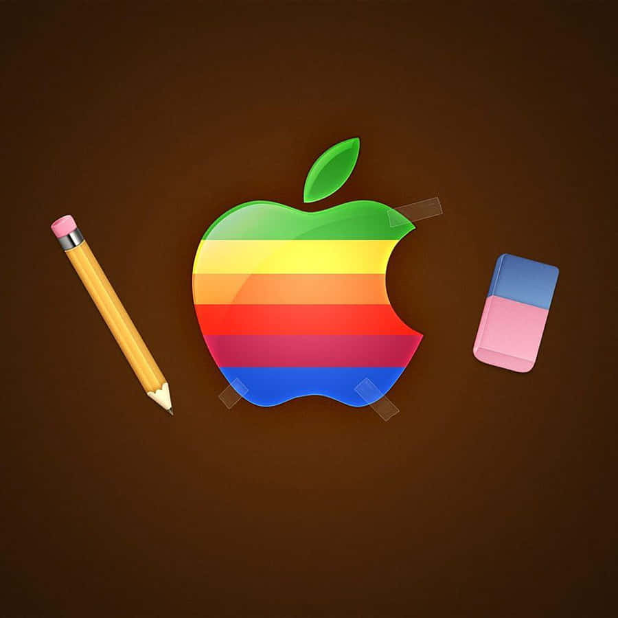 復古蘋果標誌 壁紙 — 一個彩虹條紋的Apple標誌用膠帶貼在棕色表面上，附近有一支黃色鉛筆和粉紅色擦膠。