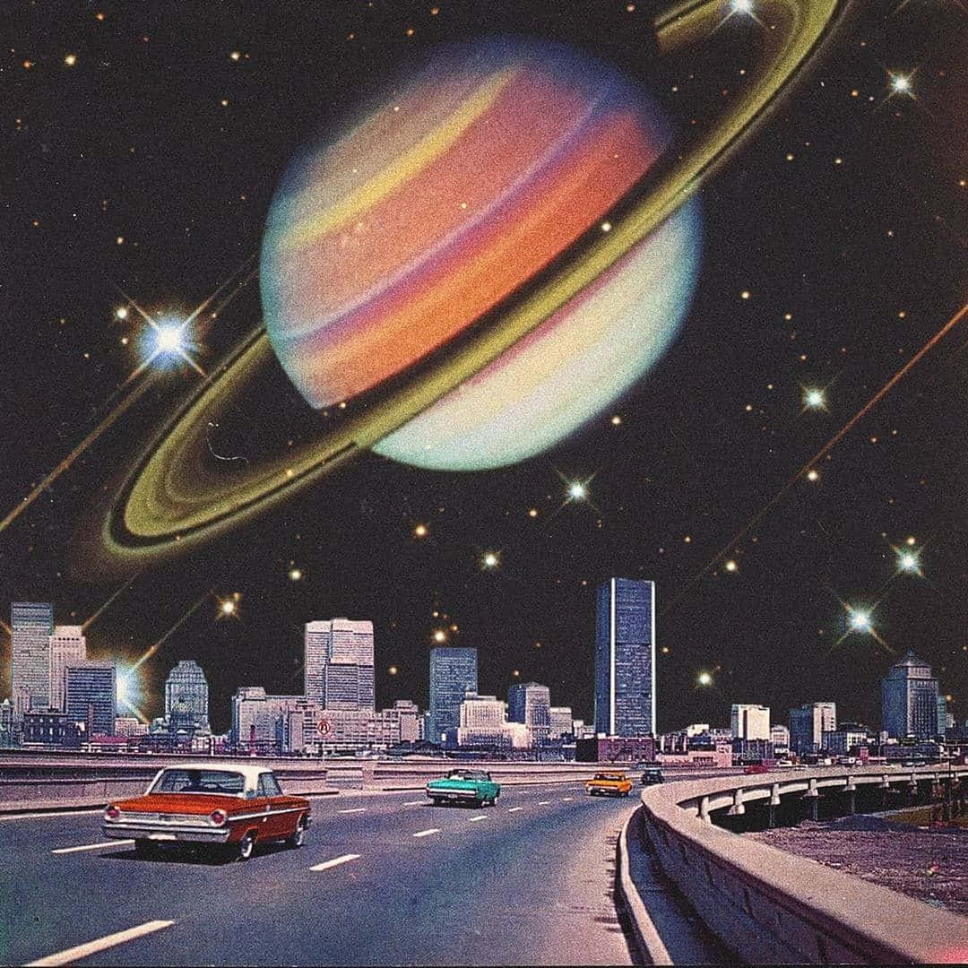 復古迷幻風格土星 壁紙 — 一條復古高速公路，經典汽車在巨大的土星下行駛，土星籠罩著夜晚未來主義的城市天際線。
