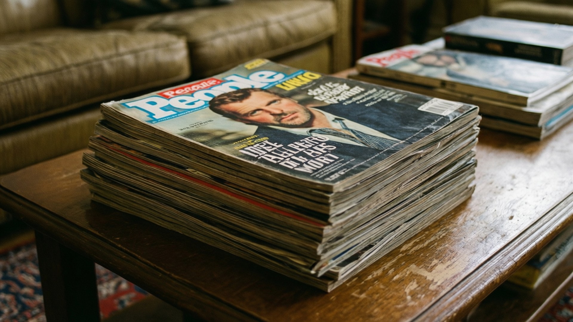 復古雜誌堆疊 壁紙 — 一堆破舊的People雜誌放在木製咖啡桌上，旁邊是一張皮沙發。